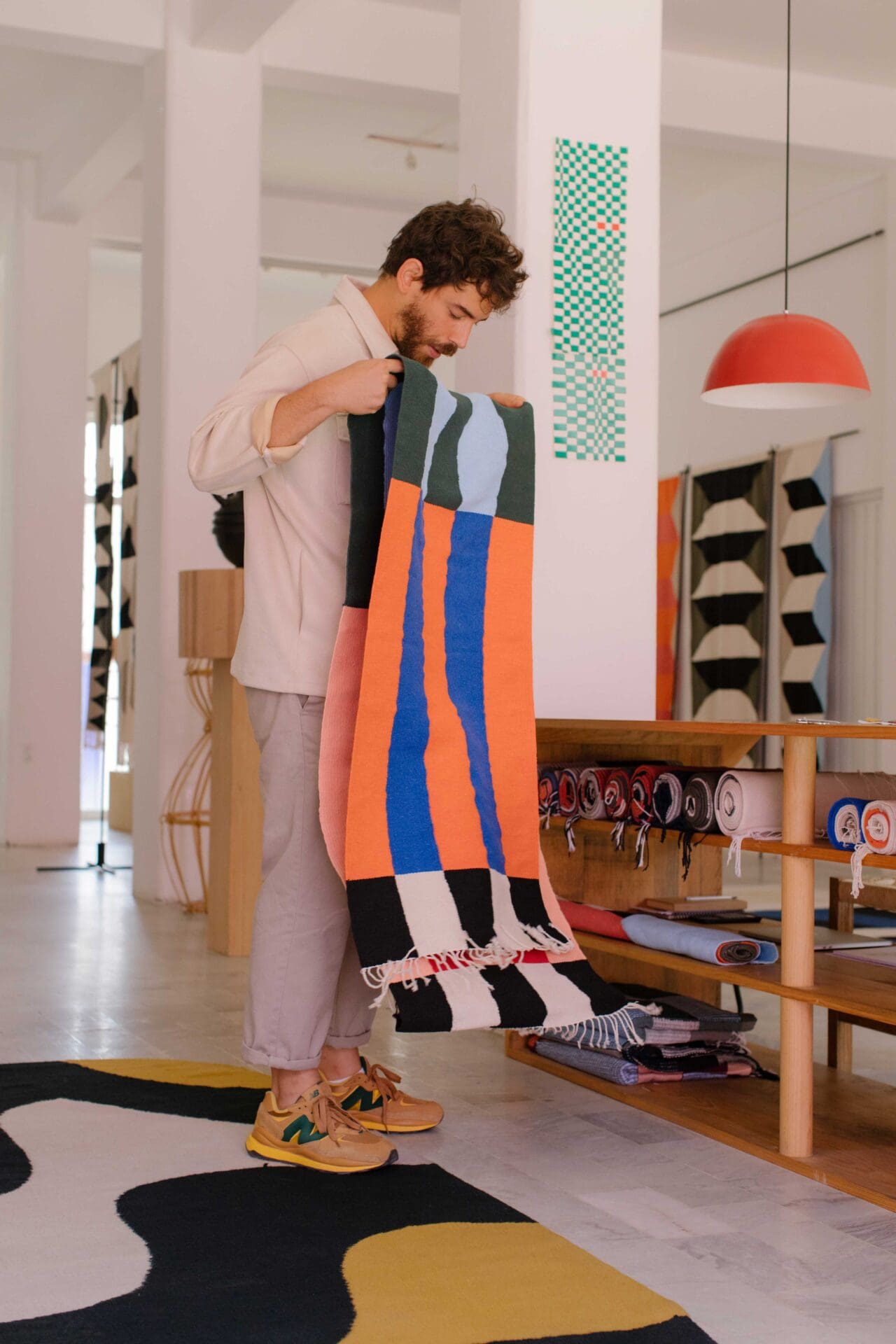Javier Reyes, rrres studio, Oaxaca | the designer folds a piece of coloured, patterned fabric in a room with a concrete floor and a graphically patterned rug