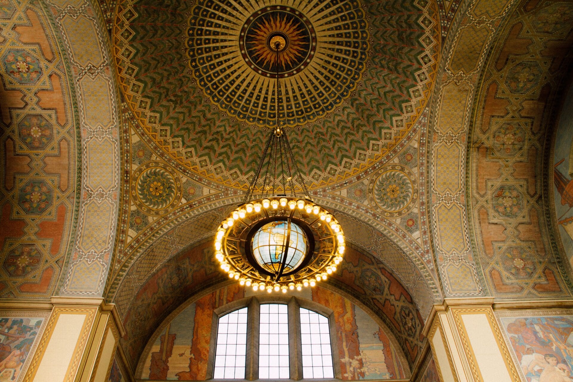 Travelling from LA to San Francisco via Amtrak train | Looking up at the ceiling of LA Union Station, will beautiful mosaics and an art deco light installation of a globe framed by globe lights