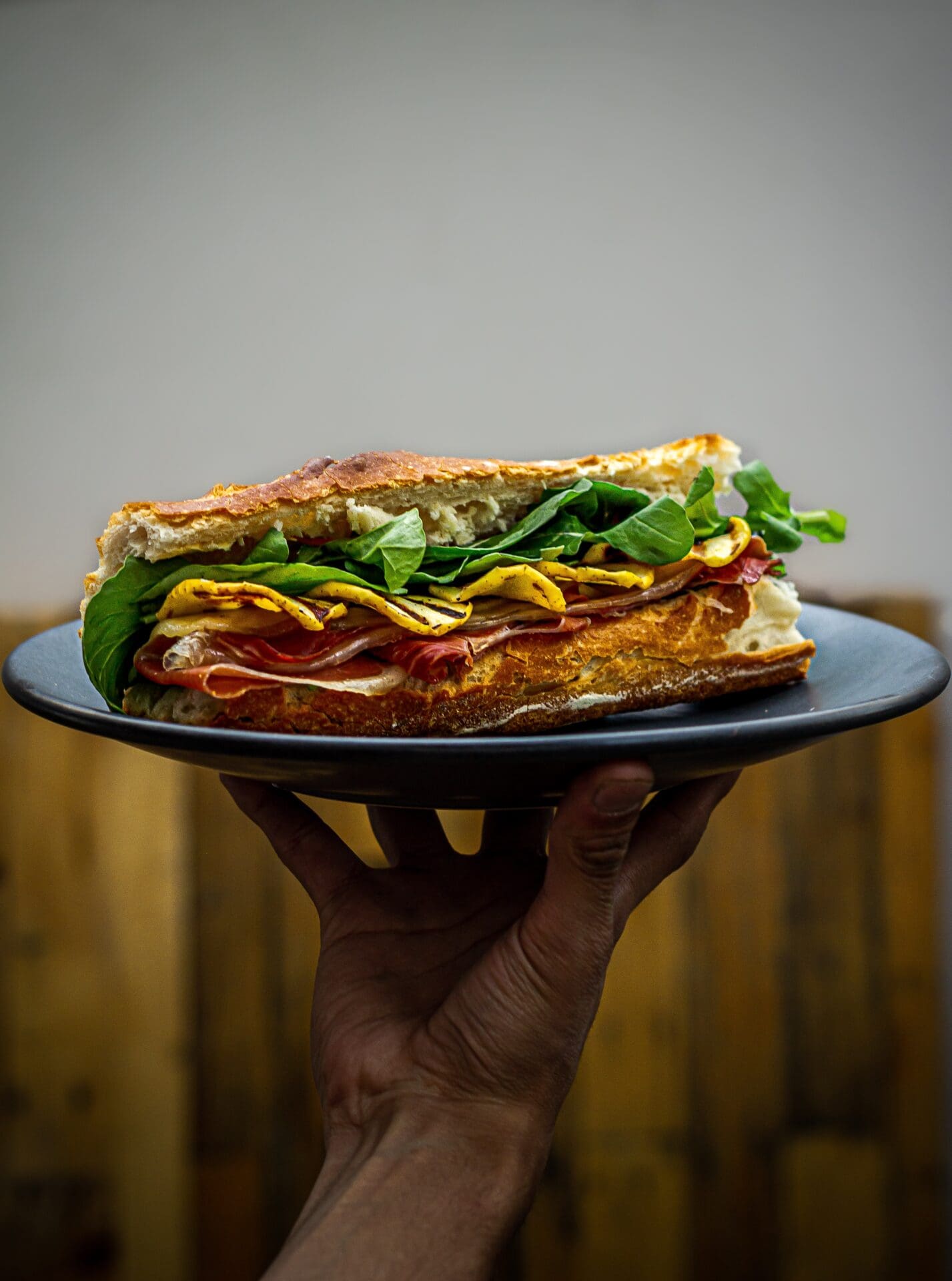 A local's guide to Mexico City | A hand holds a grey plate, on which rest a sandwich made with baguette, filled with cured meat and greens