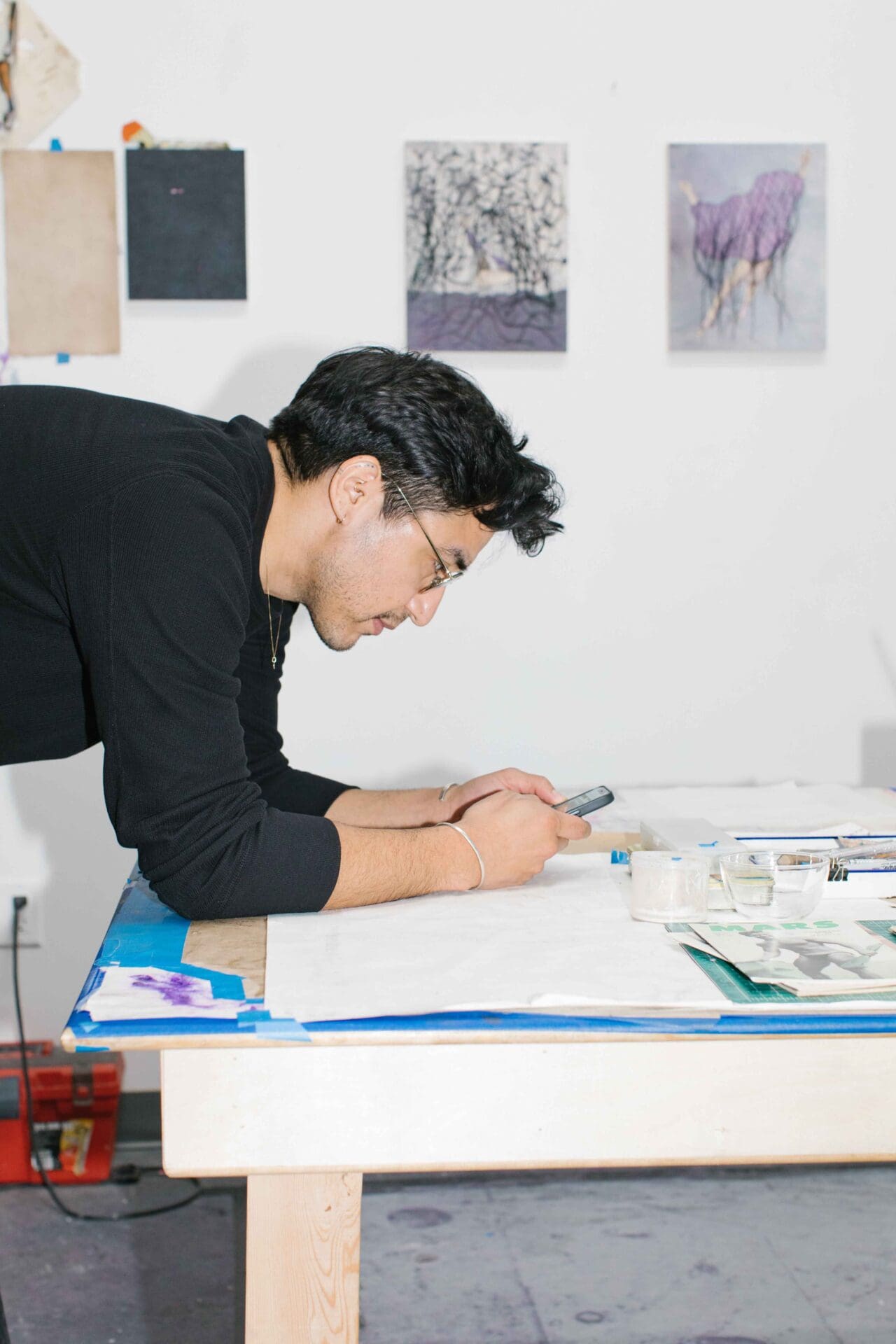 Felipe Baeza | Felipe Baeza leans on a desk looking at his phone inside his studio.