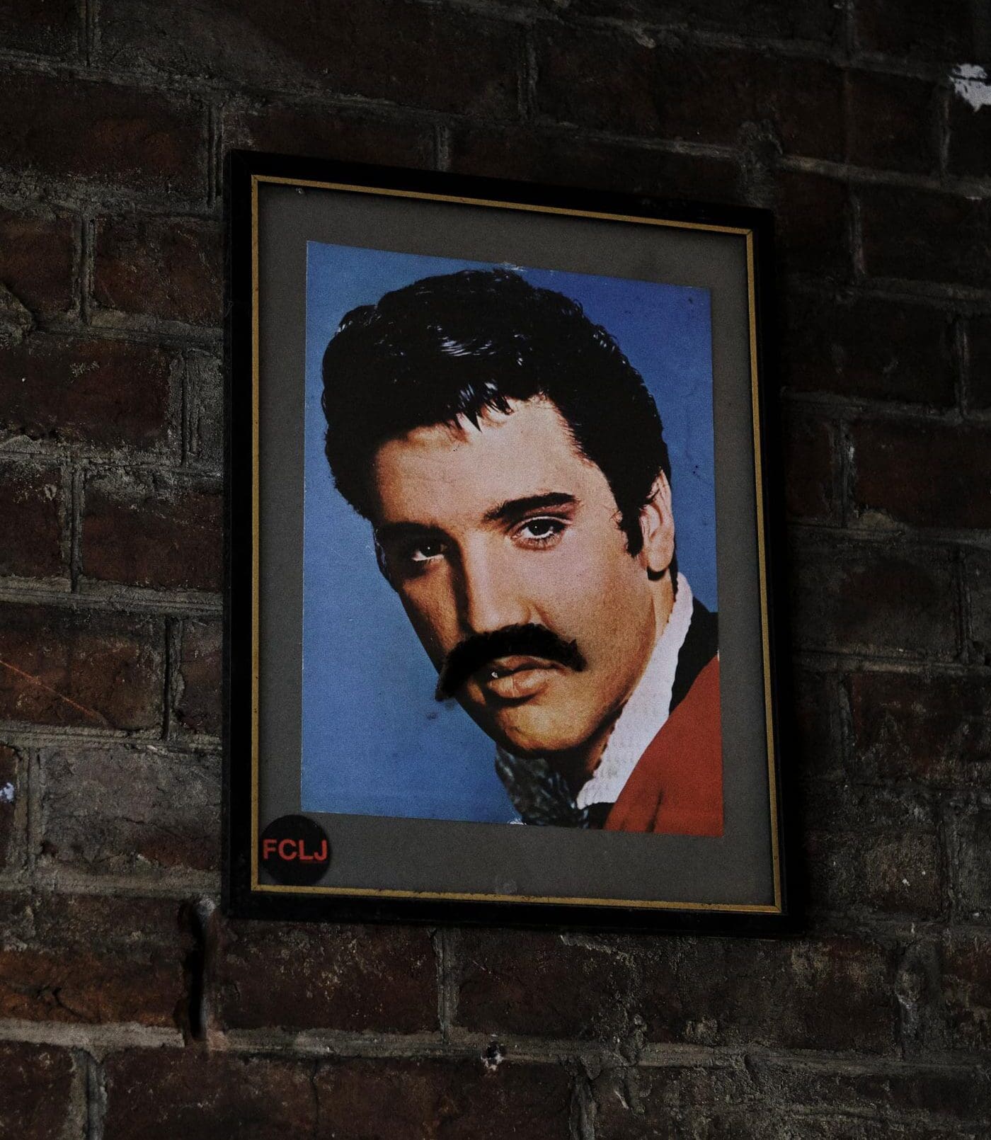 A weekend in Hastings | A photo of Elvis Presley with a fake moustache on, mounted to a brick wall inside Dragon Bar in Hastings