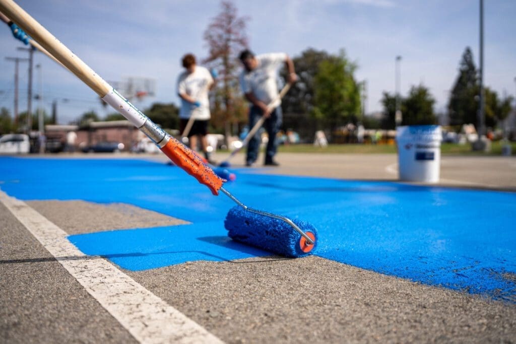 The LA neighbourhood using reflective paint to tackle rising temperatures | A close-up shot of a paint roller spreading blue reflective paint over a school playground in Pacoima, Los Angeles.