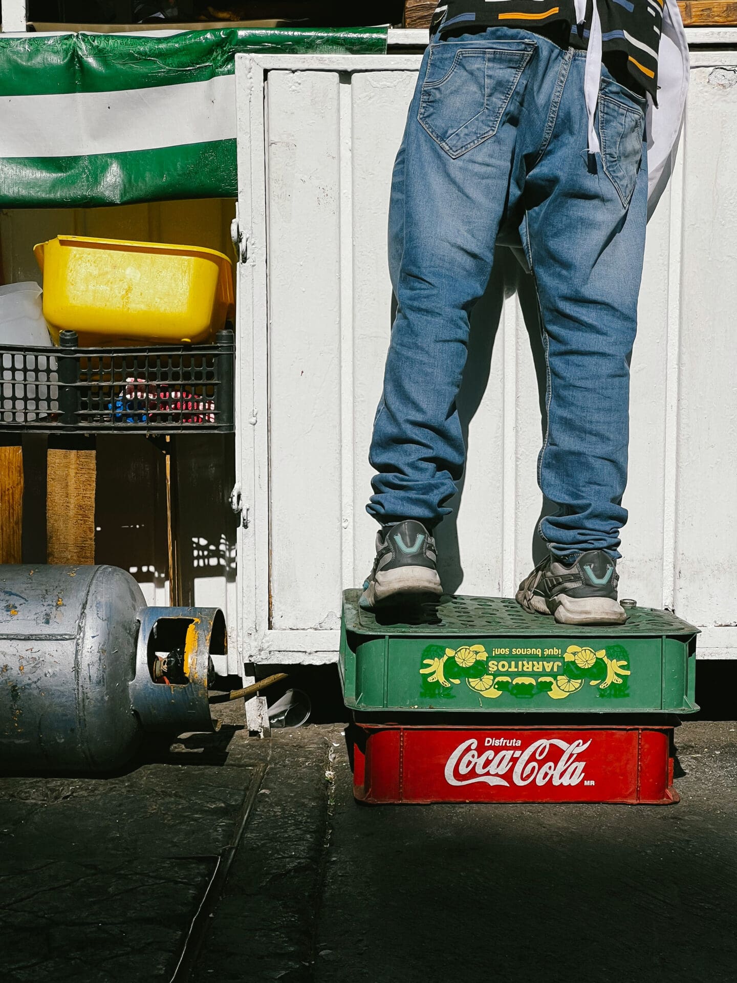 Photographer Manuel Zúñiga on Mexico City | Someone wearing jeans and trainers stands on a red plastic Coca Cola crate and a green crate stacked on top of each other