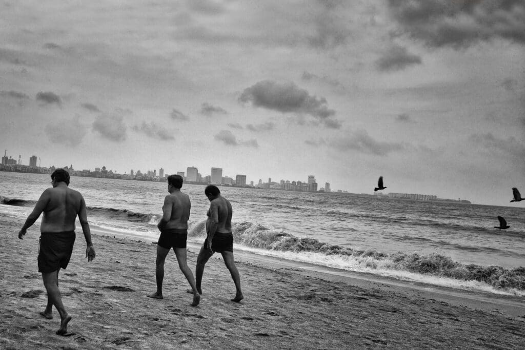 Photographer Sunhil Sippy on Mumbai | Three men wearing swimming trunks walk along the beach, away from the camera