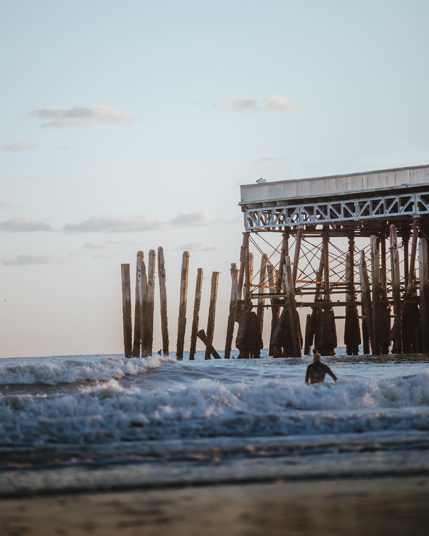 A weekend in Hastings | a view of the waves at the beach with a surfer in the mid distance, and the pier reaching overhead from the right