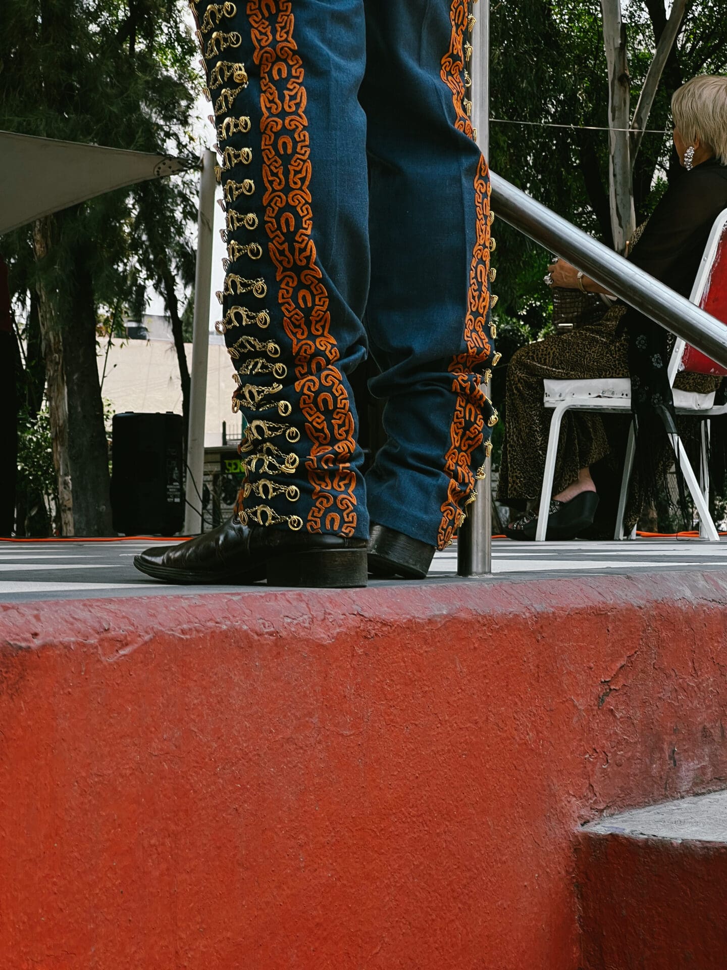 Photographer Manuel Zúñiga on Mexico City | a man wearing classic Mexican trousers, blue and with orange and yellow patterns, stands on a red-painted wall