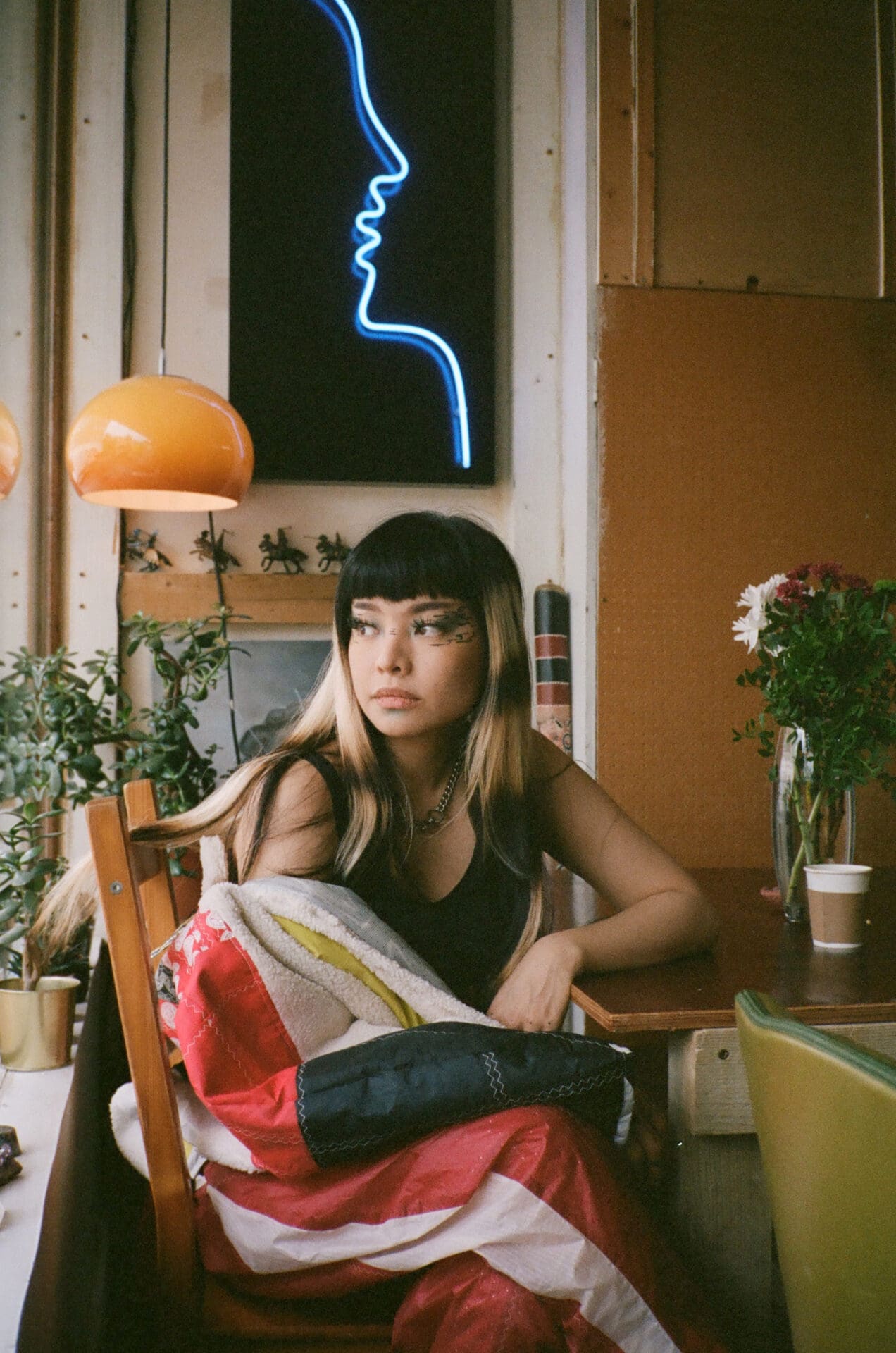 An interview with Thai pop singer Pyra | Pyra sat in a chair below a vintage light shade and neon art work.