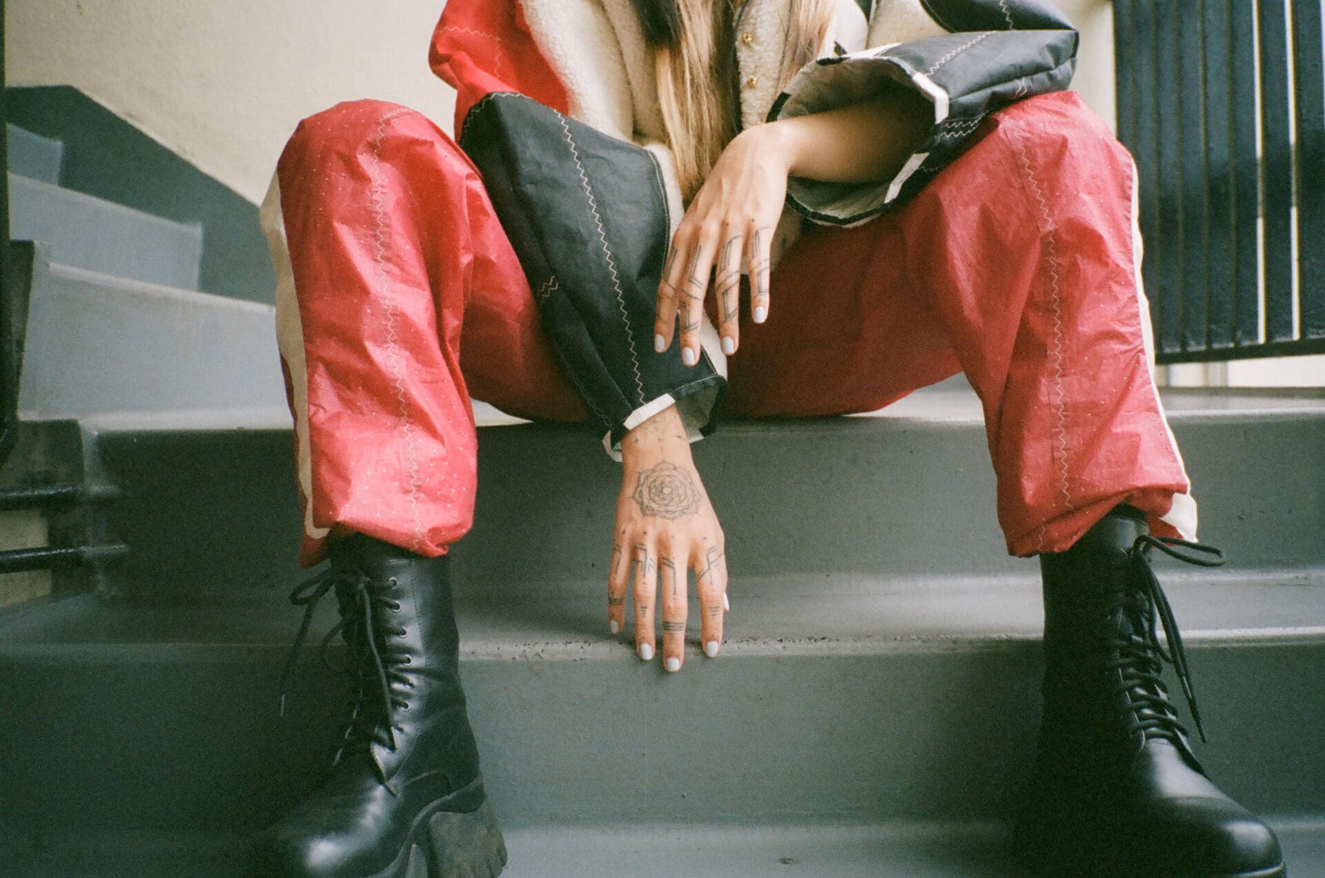 An interview with Thai pop singer Pyra | Pyra sat on metal stairs, with her red trousers, black lace up boots, and hand design visible.