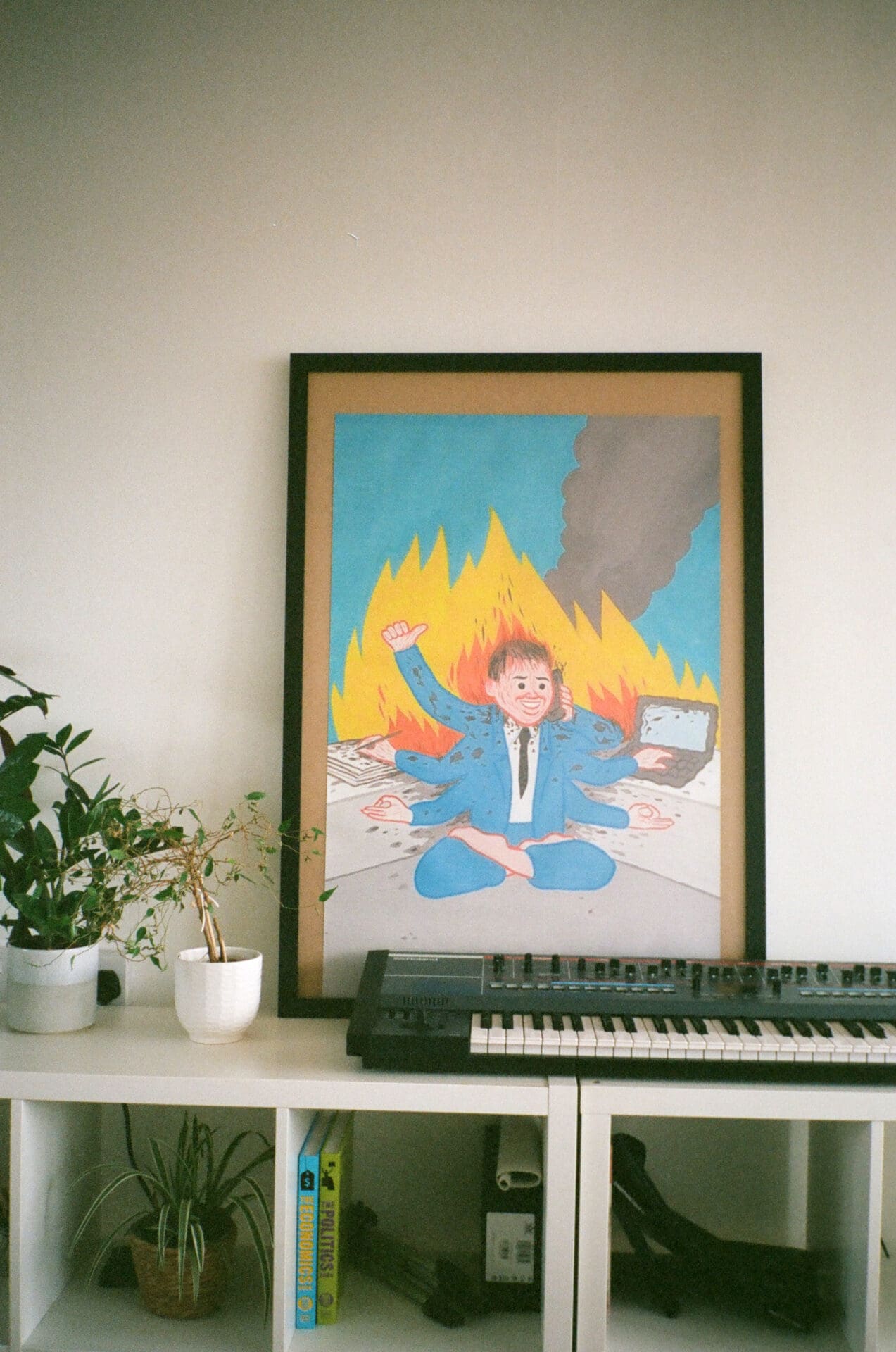 An interview with Thai pop singer Pyra | Inside Pyra's apartment, a Juno synthesiser sits on a white shelving unit, in front of an artwork of a man in a suit on fire with six arms.