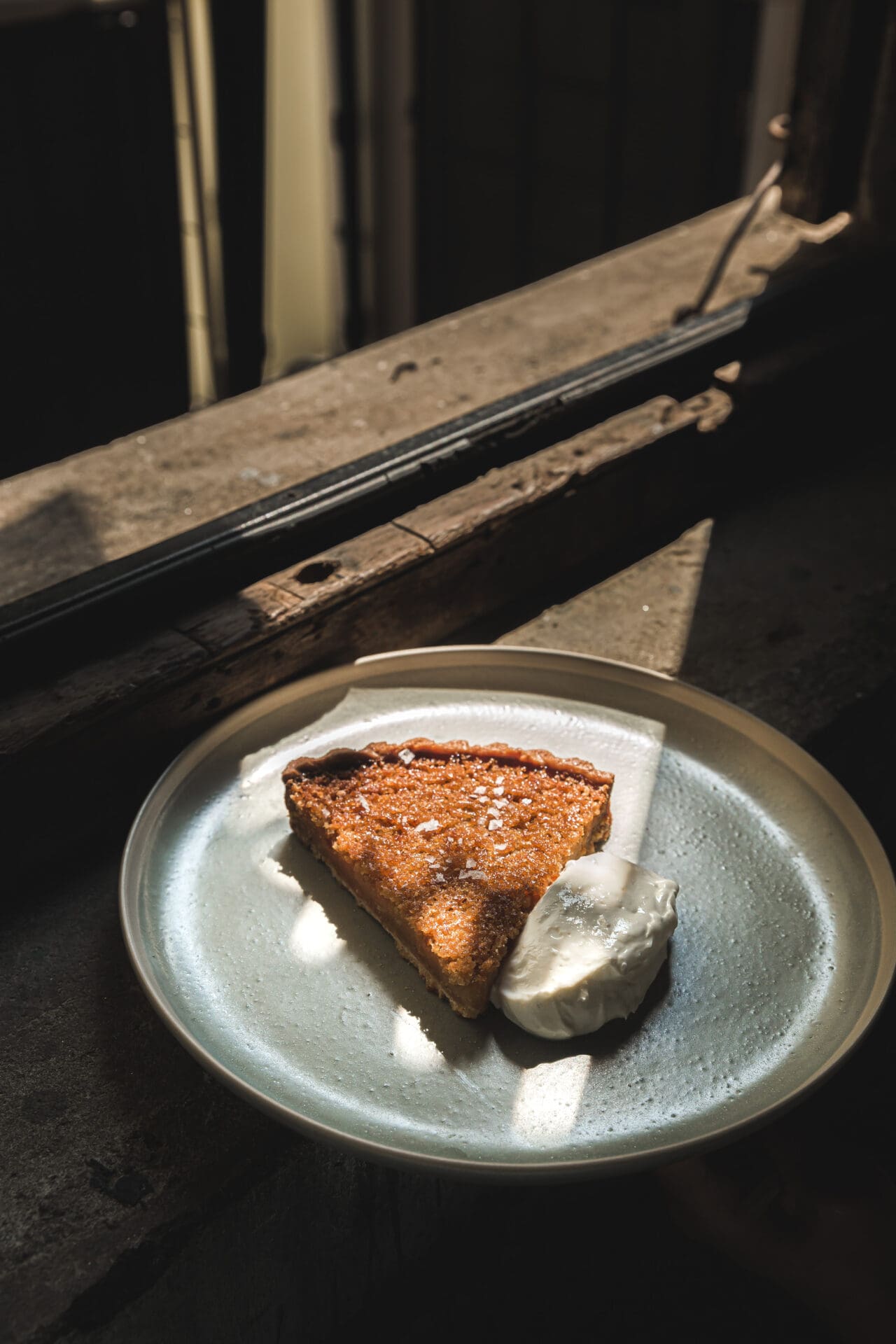 Best Bangkok coffee shops | A slice of treacle tart served with a scoop of cream sits on a window sill, with light spilling across it