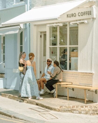 People laughing and smiling outside whitwashed Kuro Coffee, Notting Hill