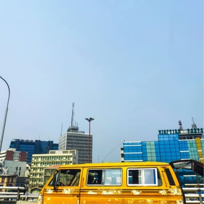 A yellow campervan cruises alongside the skyscrapers of Lagos