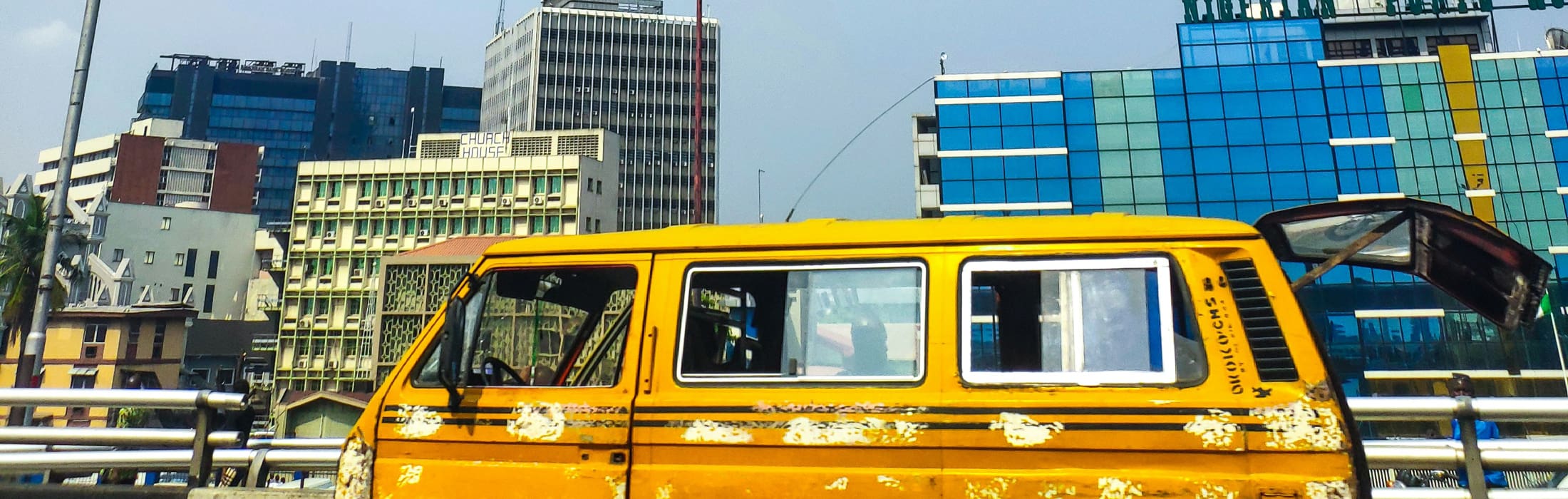 A yellow campervan cruises alongside the skyscrapers of Lagos