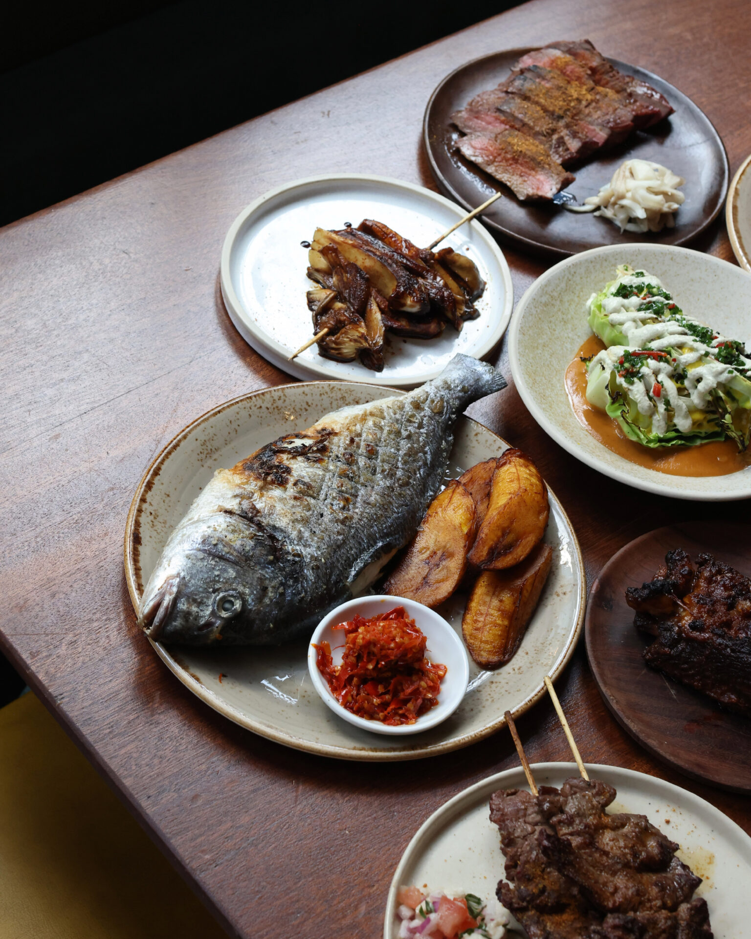 The best restaurants in Brixton, South London | A dark wood tabletop covered in plates of food, including a whole fish dish, and meat skewers, at Chishuru
