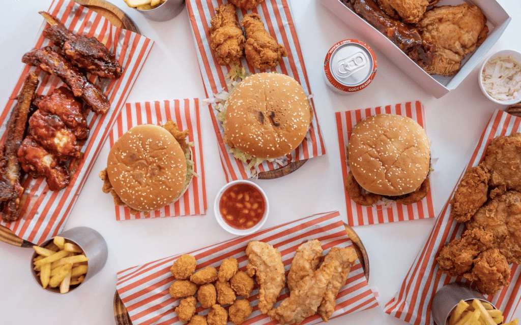 The best restaurants in Brixton, South London | Burgers, fried chicken, and hot wings served on red and white striped paper on a white tabletop in Morley's
