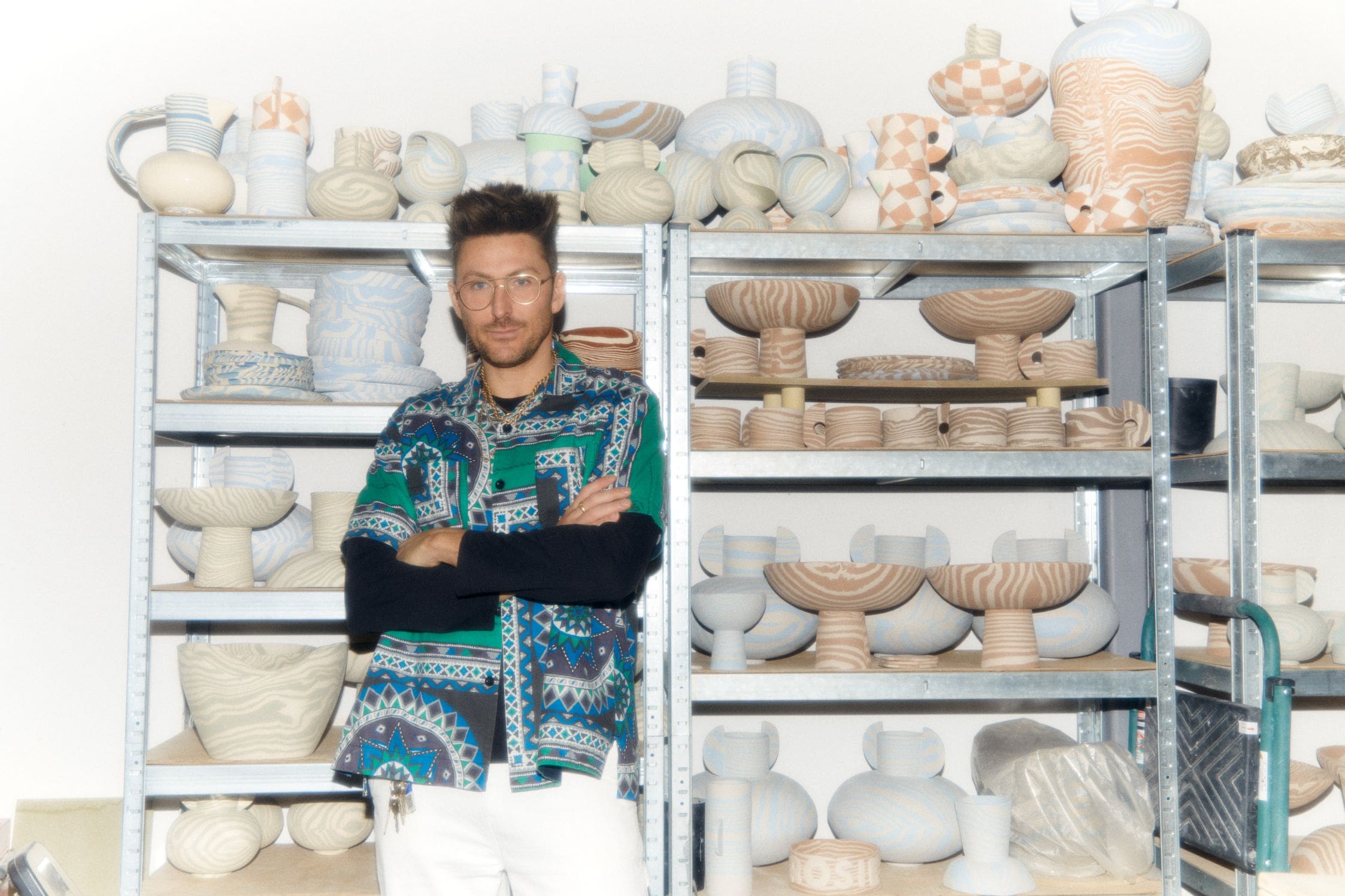 In the studio with Henry Holland | Henry Holland standing in front of a shelf filled with pots in progress in his studio.
