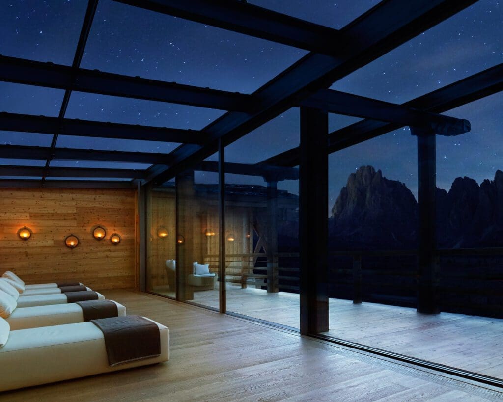 The most spectacular places to stay in the Alps this winter | A spa area with a glass roof and wall to view the night sky outside Adler Mountain Lodge in the Alpe di Siusi