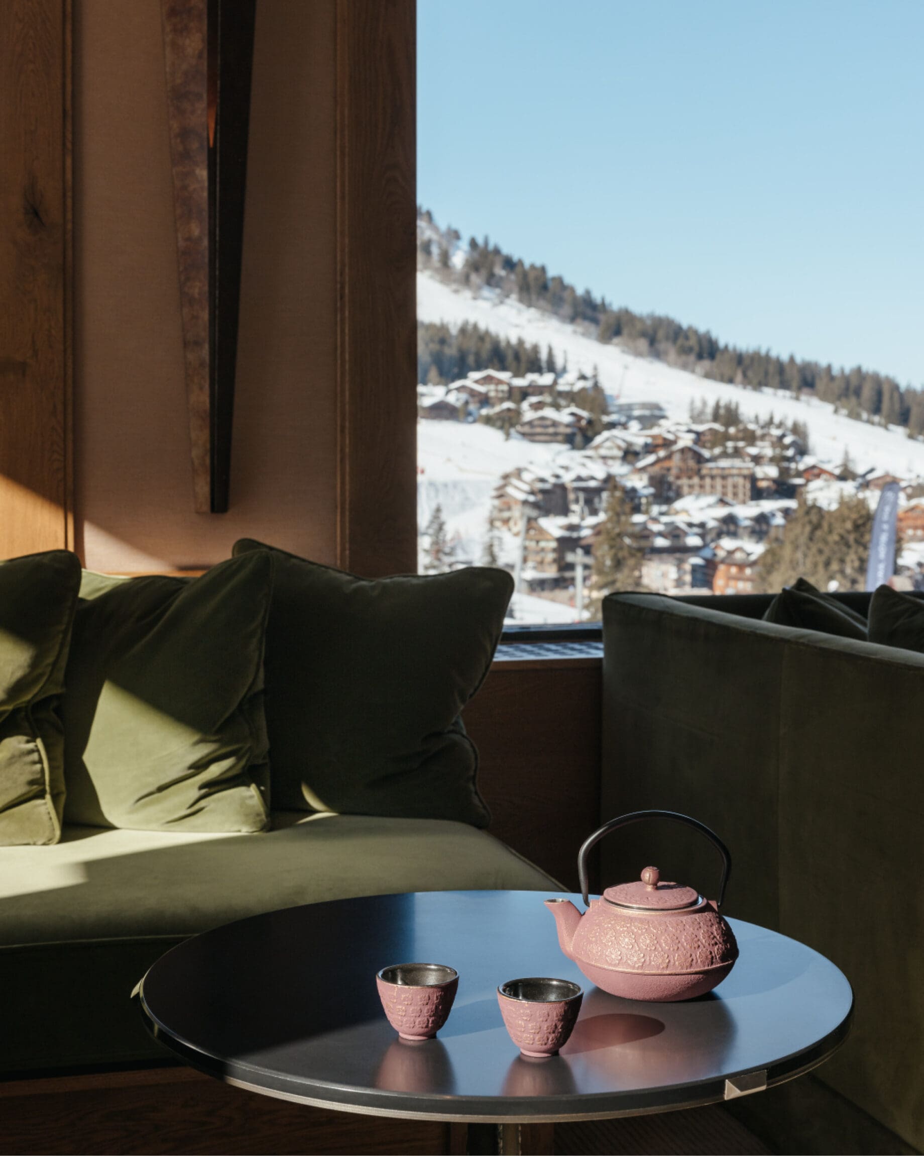 The most spectacular places to stay in the Alps this winter | Sunlight falls across a green sofa and a pink tea pot and two cups inside Aman Le Melezin