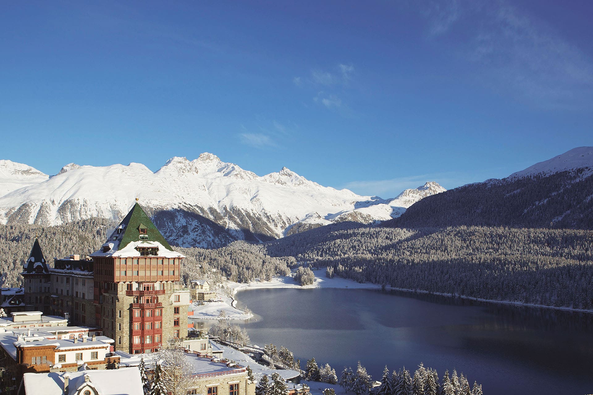 The most spectacular places to stay in the Alps this winter | Badrutt's Palace overlooking Lake St Moritz, with a snowy mountain in the background