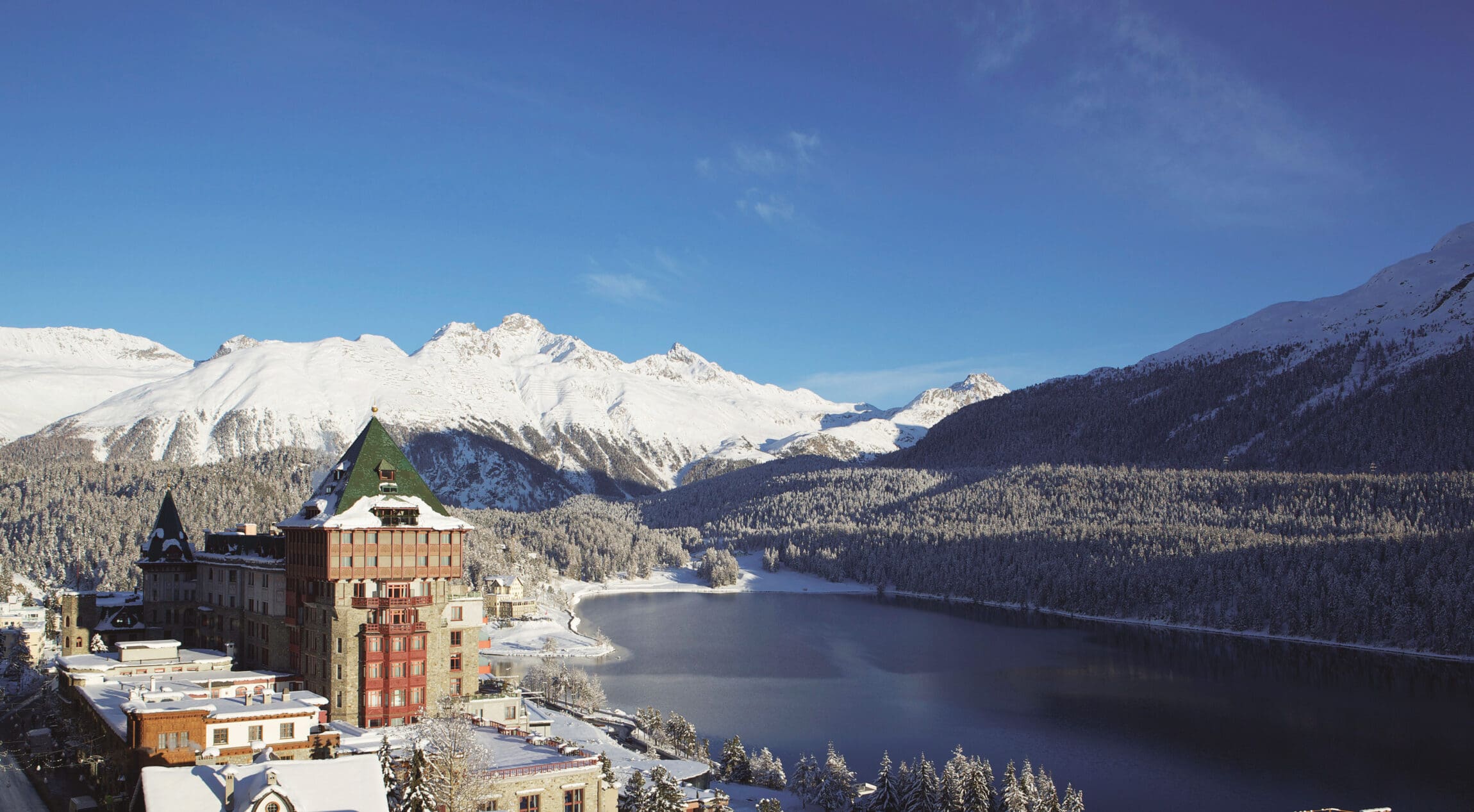 The most spectacular places to stay in the Alps this winter | Badrutt's Palace overlooking Lake St Moritz, with a snowy mountain in the background