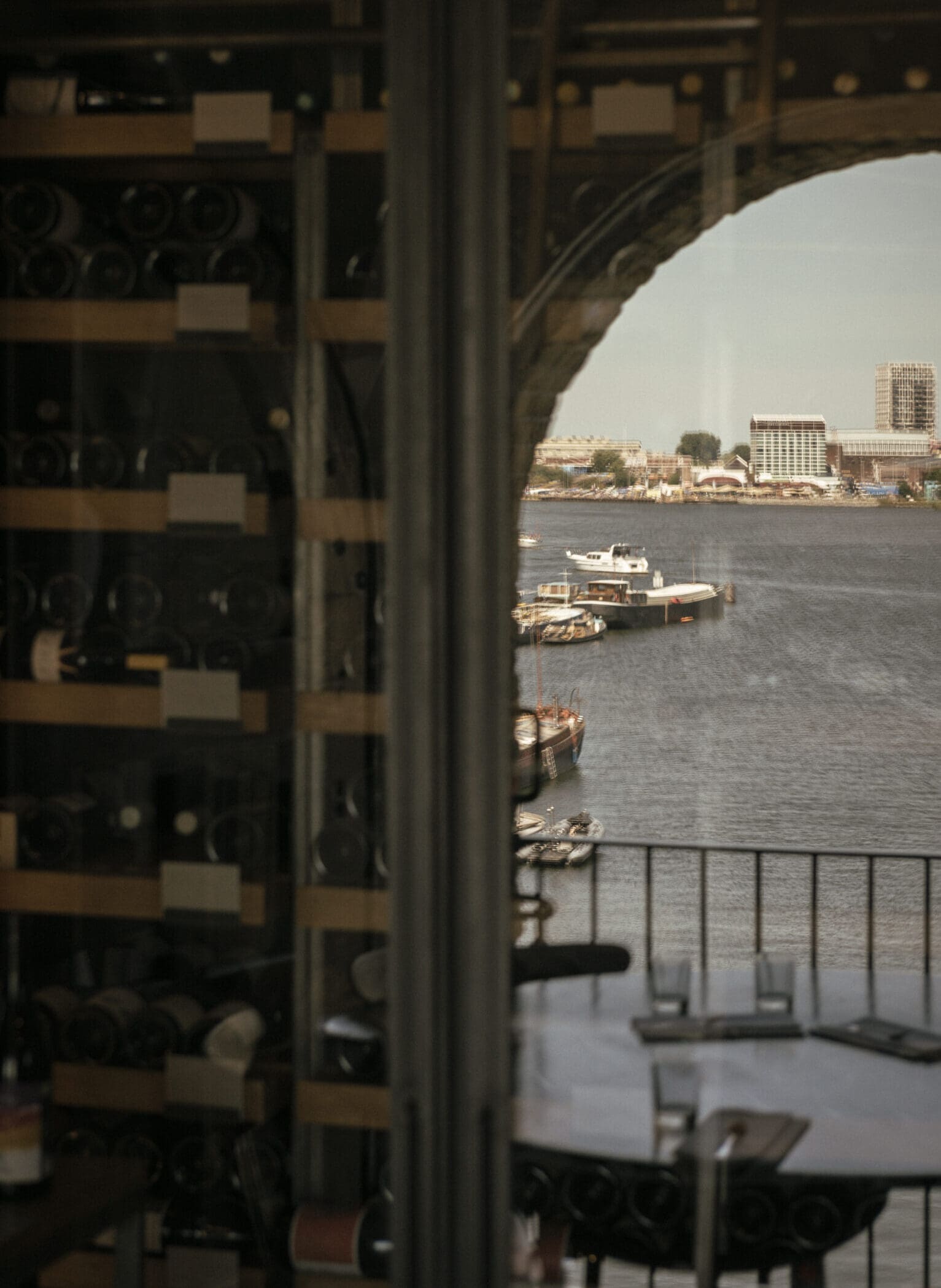 The best restaurants in Amsterdam | Wine bottles are lined along the wall next to a window overlooking the grey blue waterfront.