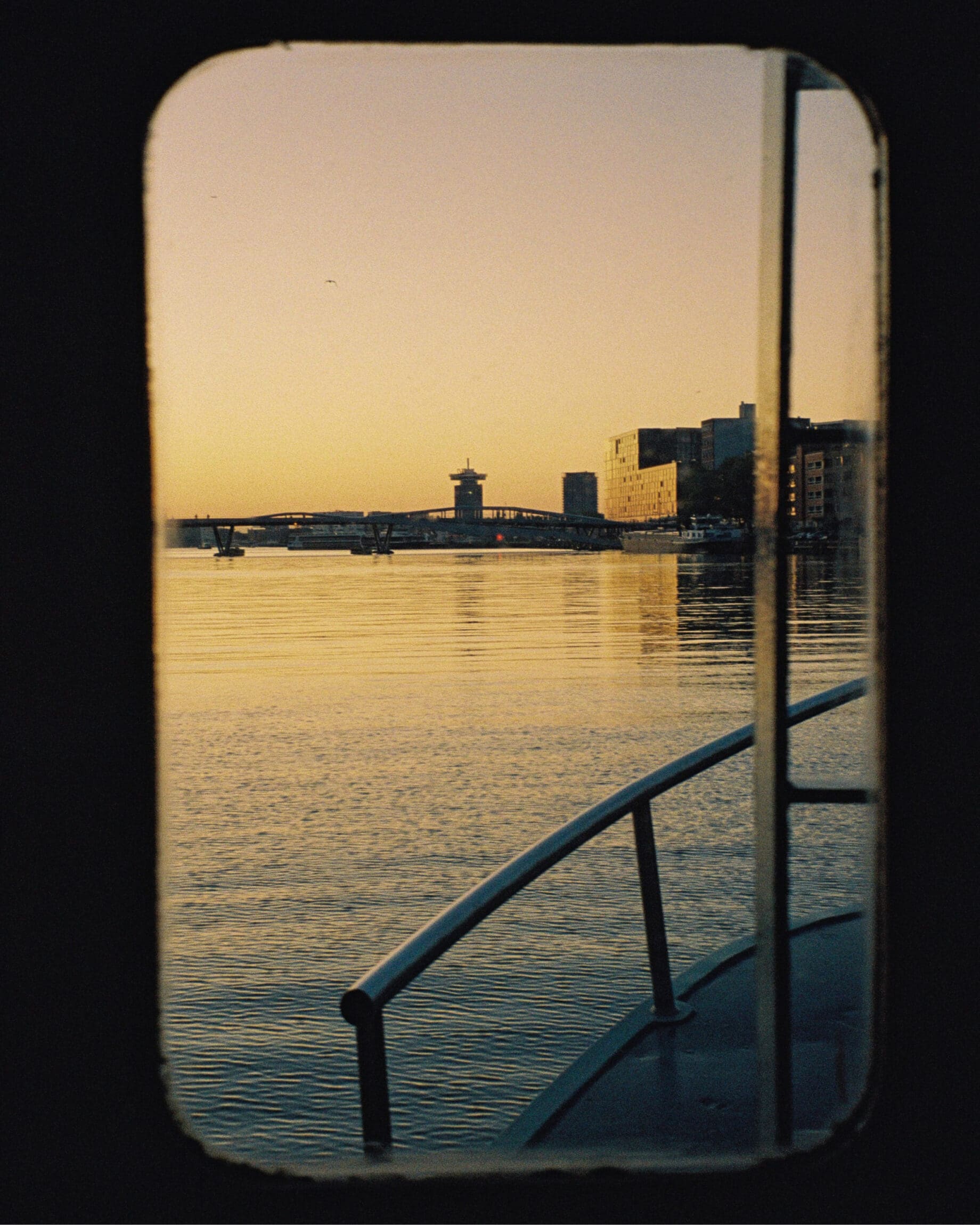 My city: Amsterdam | Boat window overlooks sun setting over eh waterfront.