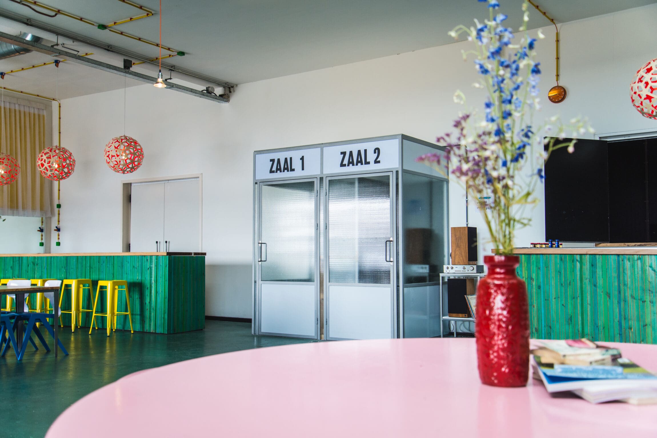 The best restaurants in Amsterdam | A circular pink table with a red vase and flowers sits in the foreground in front of a green bar.