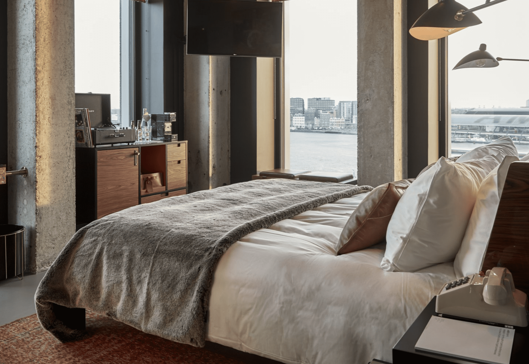 The best hotels in Amsterdam | This Sir Adam Hotel room is lined with cement walls with floor to ceiling windows that overlooks the water.