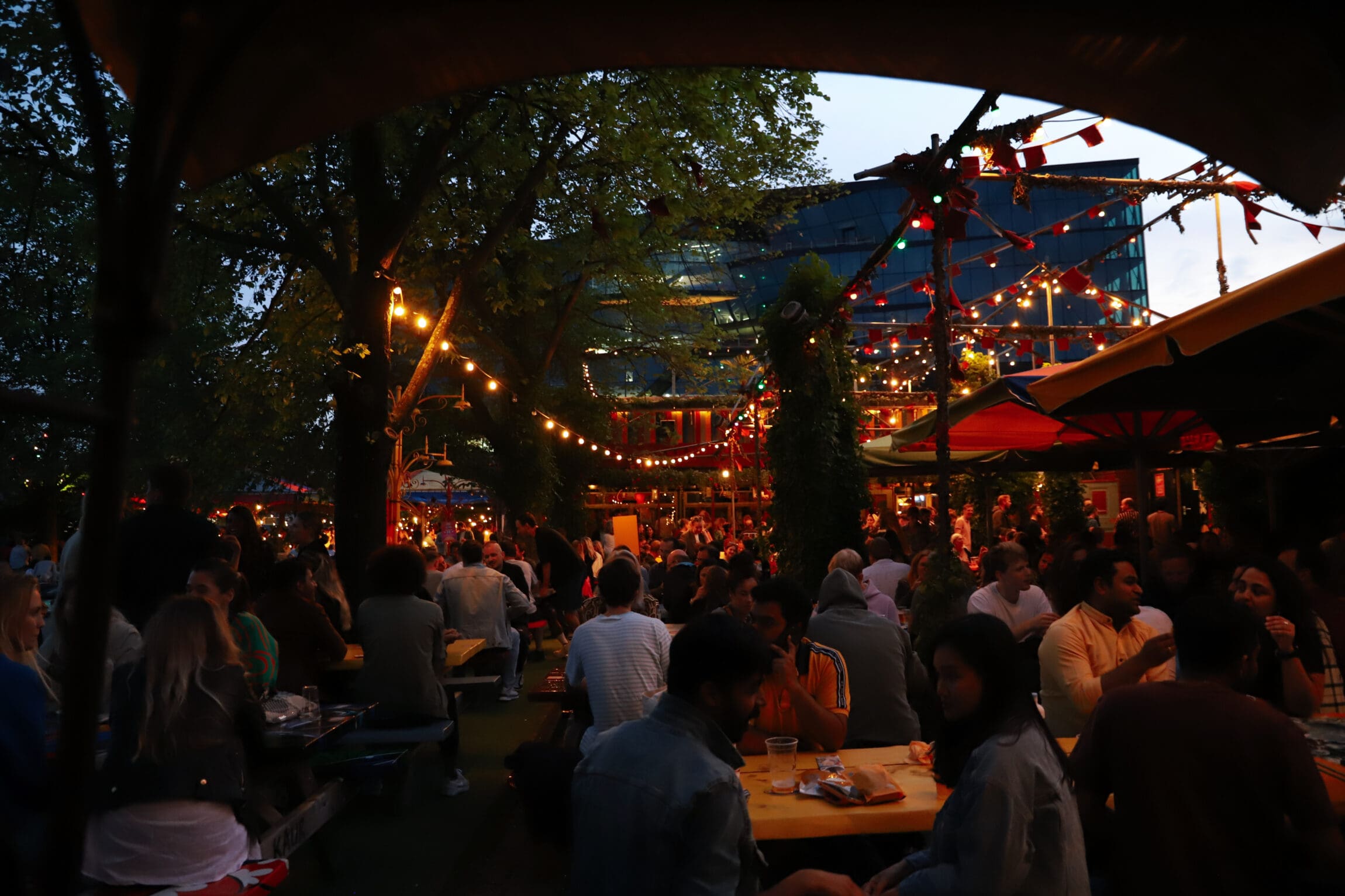 The best bars in Amsterdam | People sit around tables outside under string lights and red canopies.
