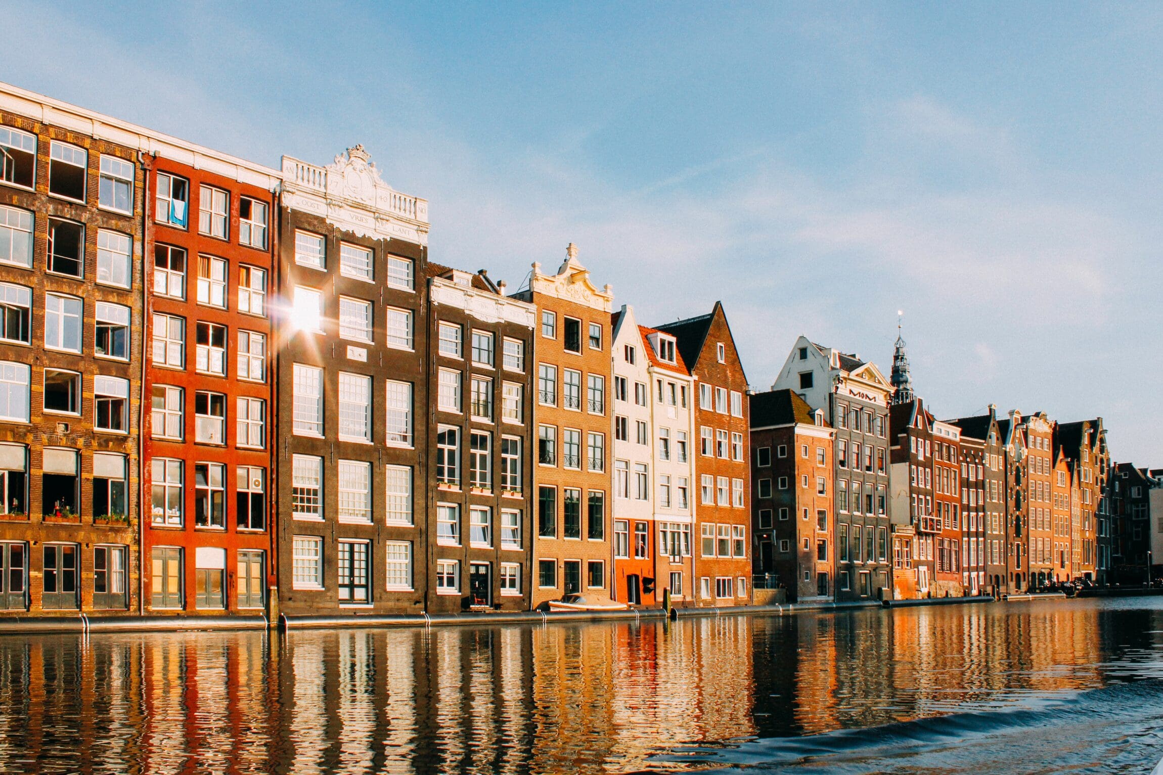 Amsterdam city guide | Orange, brown, and white row houses reflect along the canal with blue skies