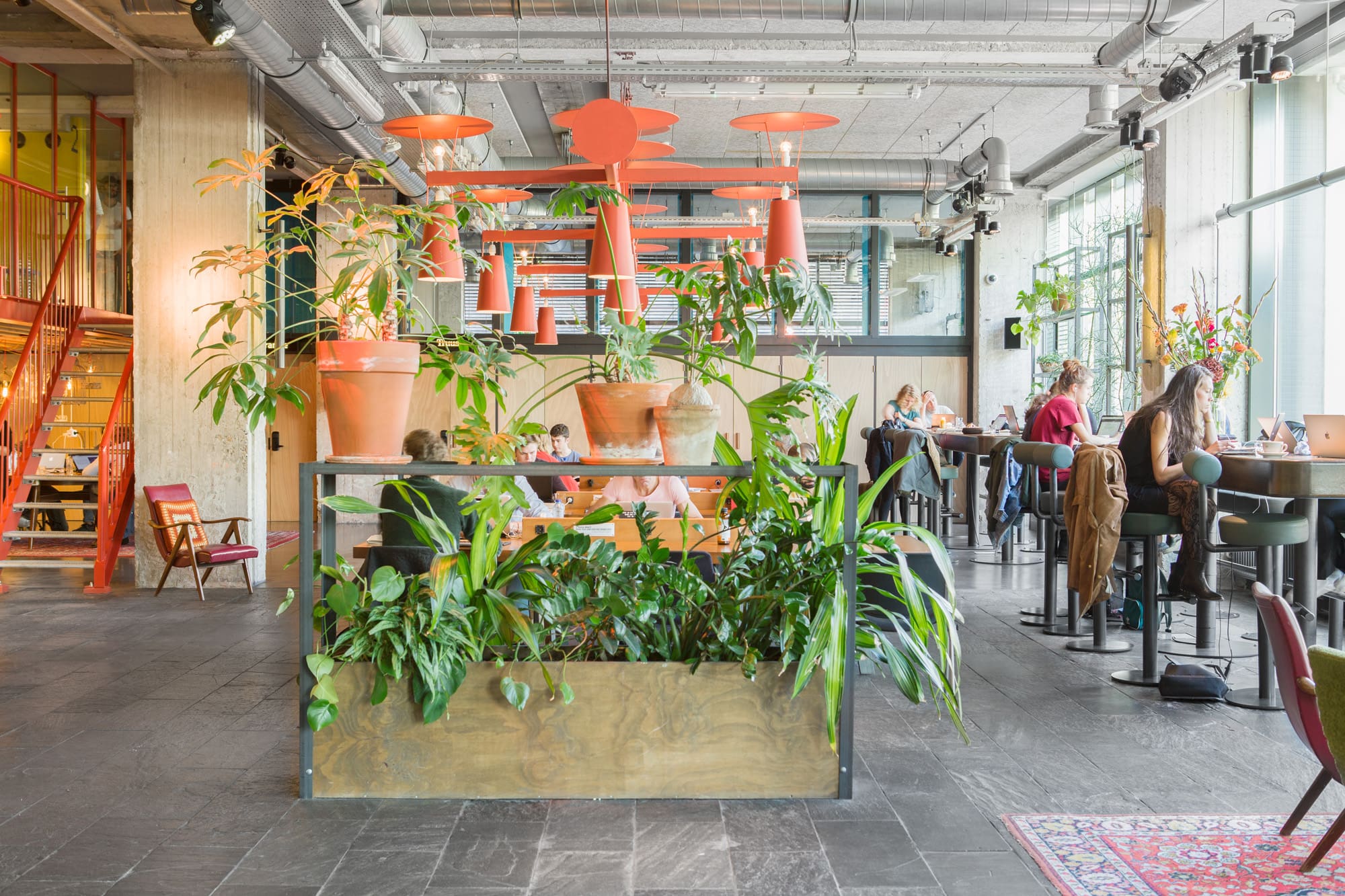 The best co-working spaces in Amsterdam for remote working | Orange lamps hang over a plant bed with people working in the background.
