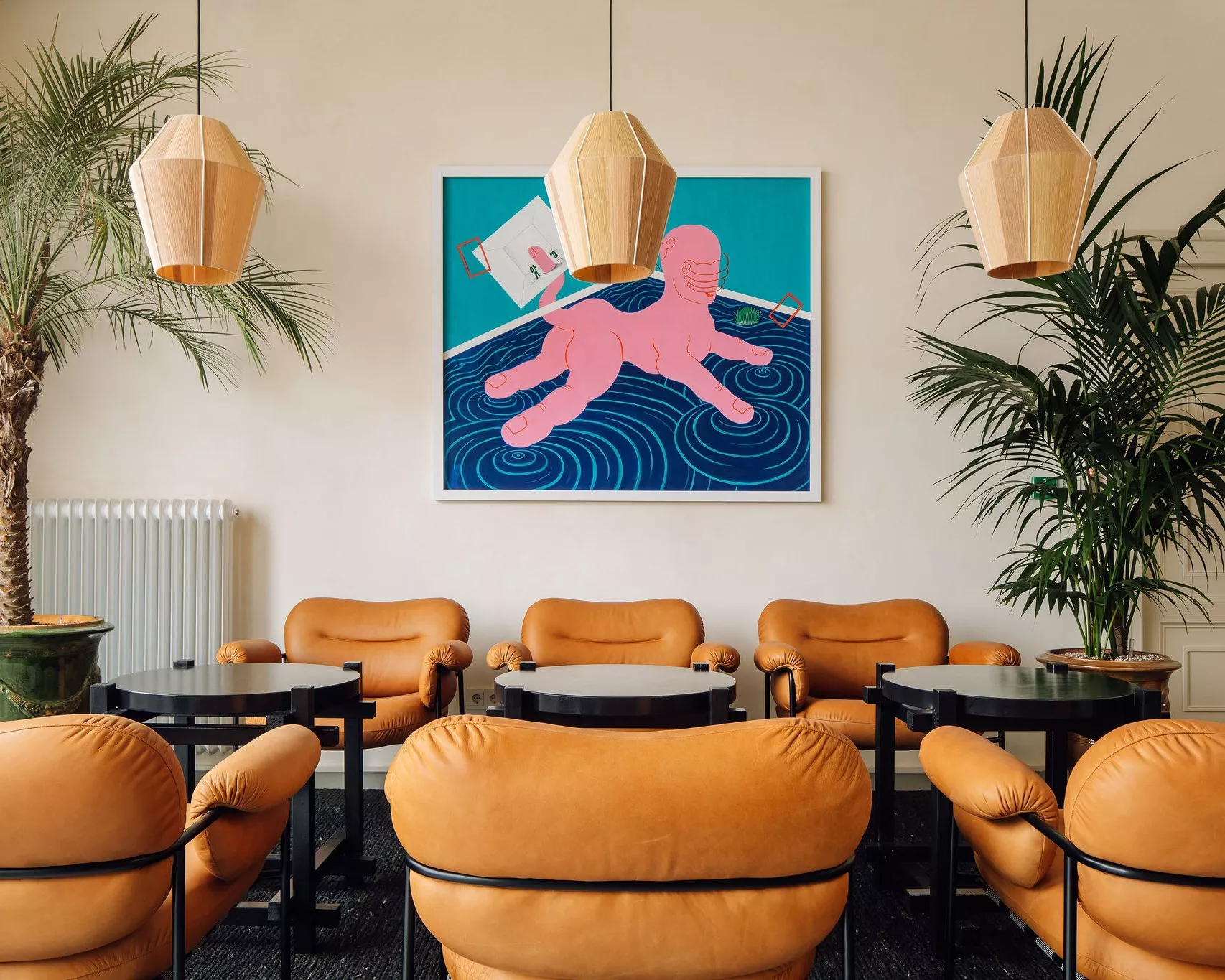 The best co-working spaces in Amsterdam for remote working | Orange arm chairs with black tables with a pink and blue painting on the wall.