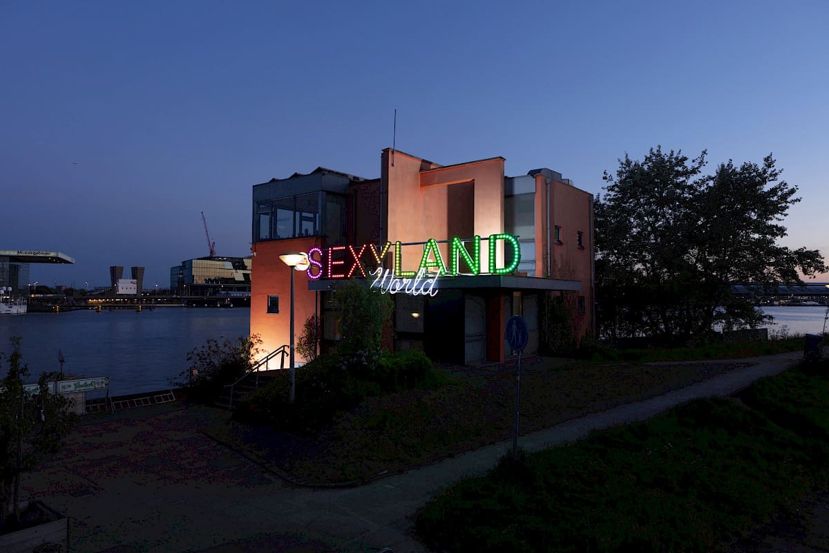 The best museums and art galleries in Amsterdam | A neon signs saying "Sexyland World" stands in front of an orange building on the waterfront at dusk.