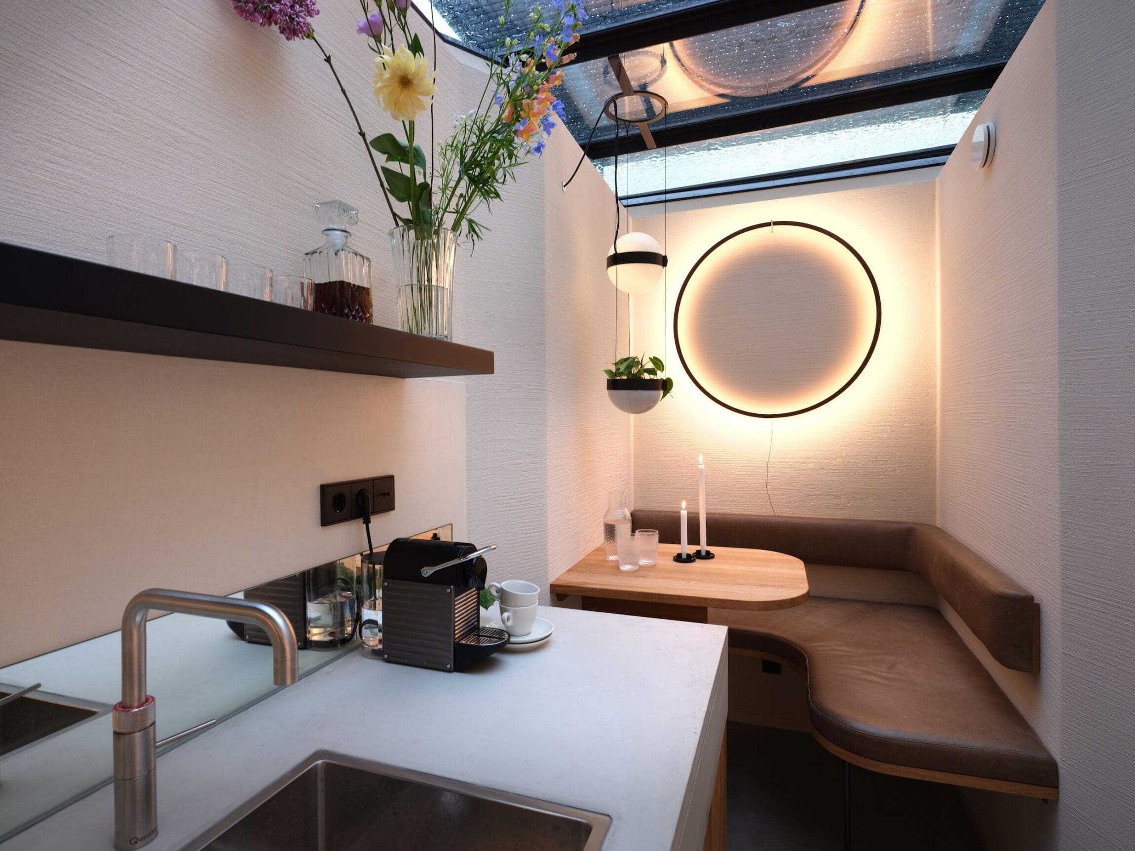 The best hotels in Amsterdam | Sitting area at the Vondice hotel with ring light mirror over a brown corner booth, a sink, and flowers.