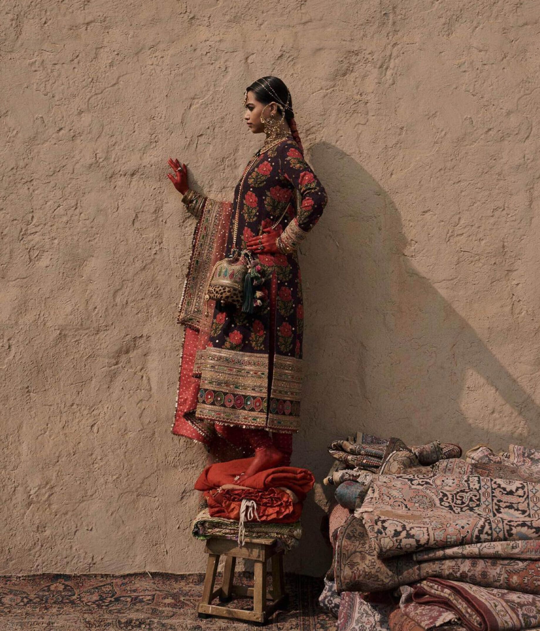 Mumbai creatives | A woman dressed in a traditional ensemble standing on a chair on top of rugs.