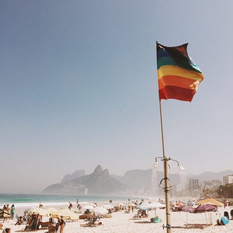 The future of queer travel | A pride flag sits in the sand on a busy beach