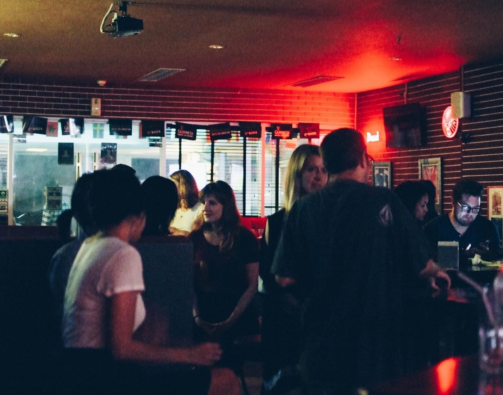 Things to do in Bangkok right now | People gathered in a dark lit room with a red neon sign in the corner