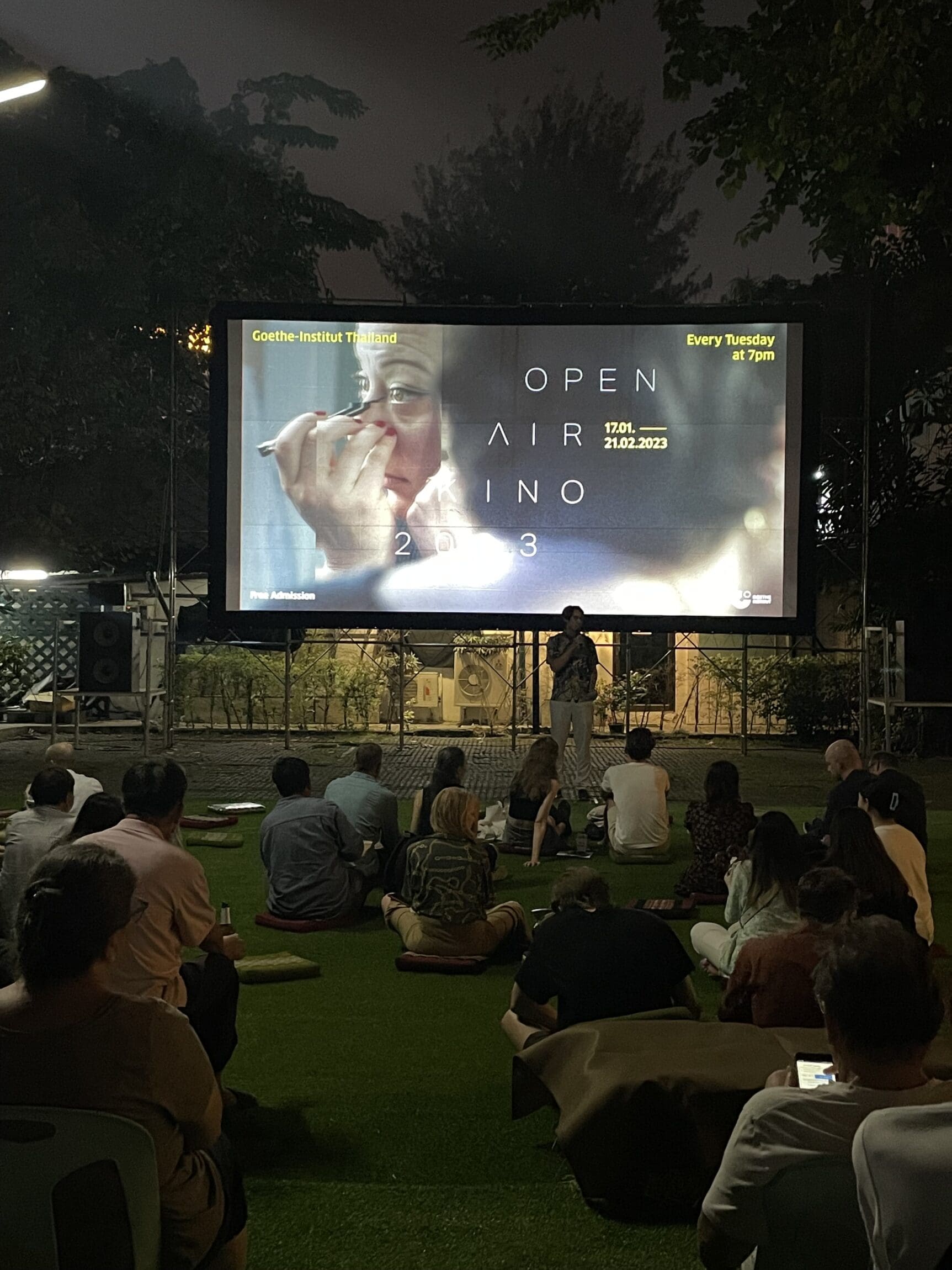 The best things to do in Bangkok right now | People sitting on a grass lawn outside looking at a large screen with the words "Open Air Kino 2023"