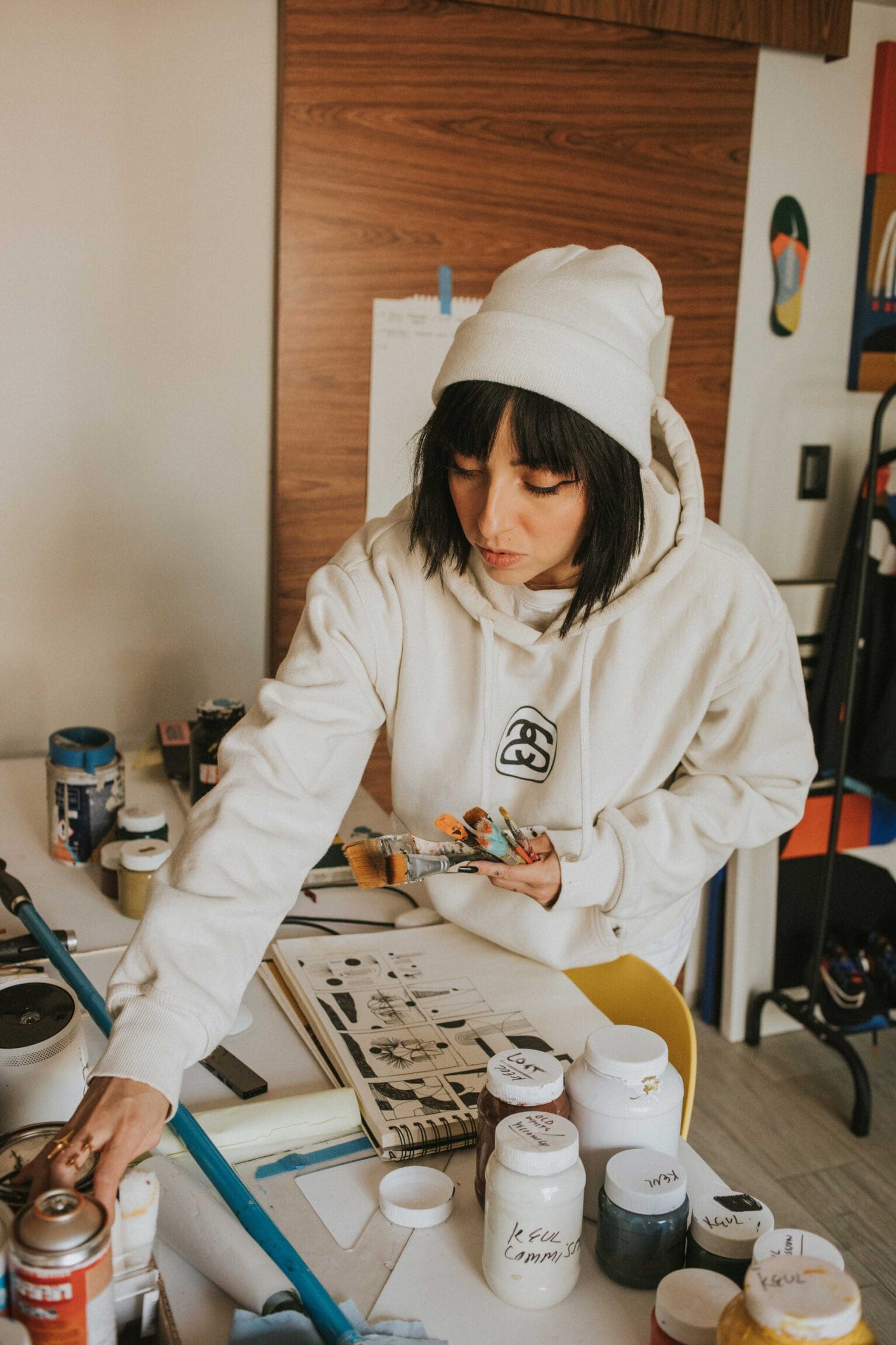Artist Luisa Salas, aka Hola Lou, shot for ROADBOOK in her home studio, choosing paint colours on a worktop, with brushes in her hand.