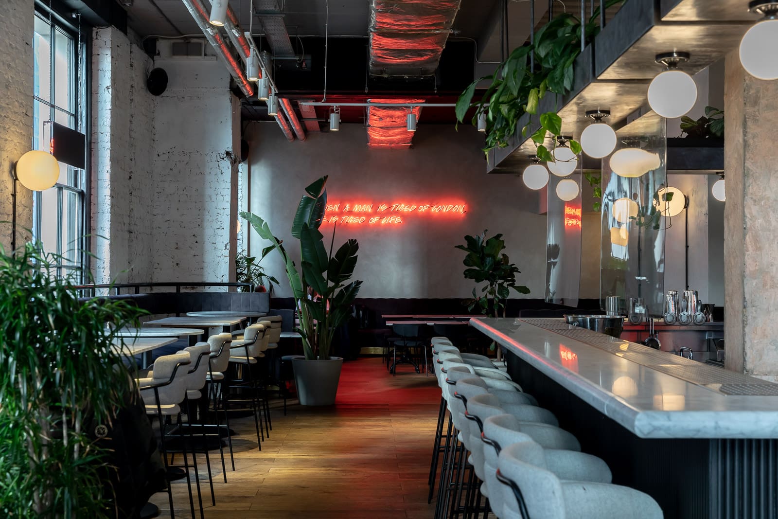 The best coffee shops in London | The inside of Grind in London Bridge has a line of chairs under a bar with greenery and a neon sign.