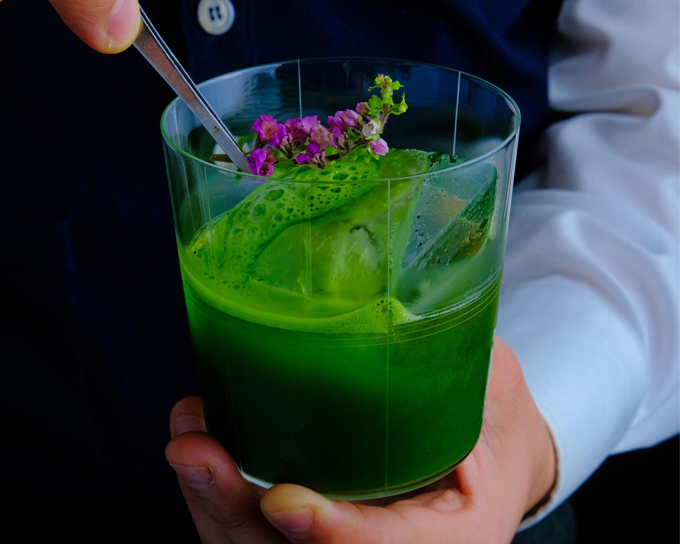 The best cocktail bars in New York City | A vibrant green cocktail garnished with a purple flower
