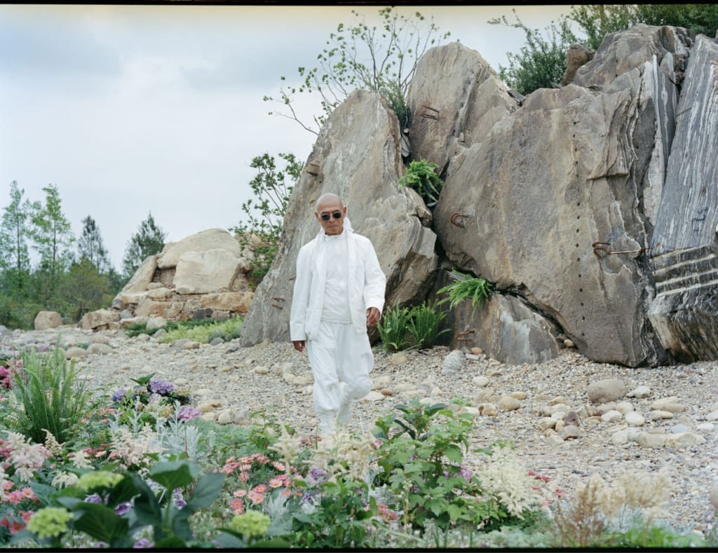 Chinese artist Zhang Huan in a white outfit against a rocky backdrop