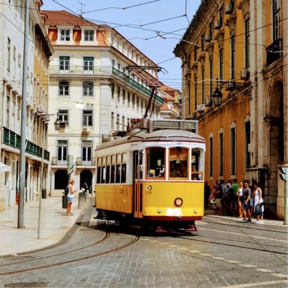 A yellow tram steers through a busy street in Lisbon