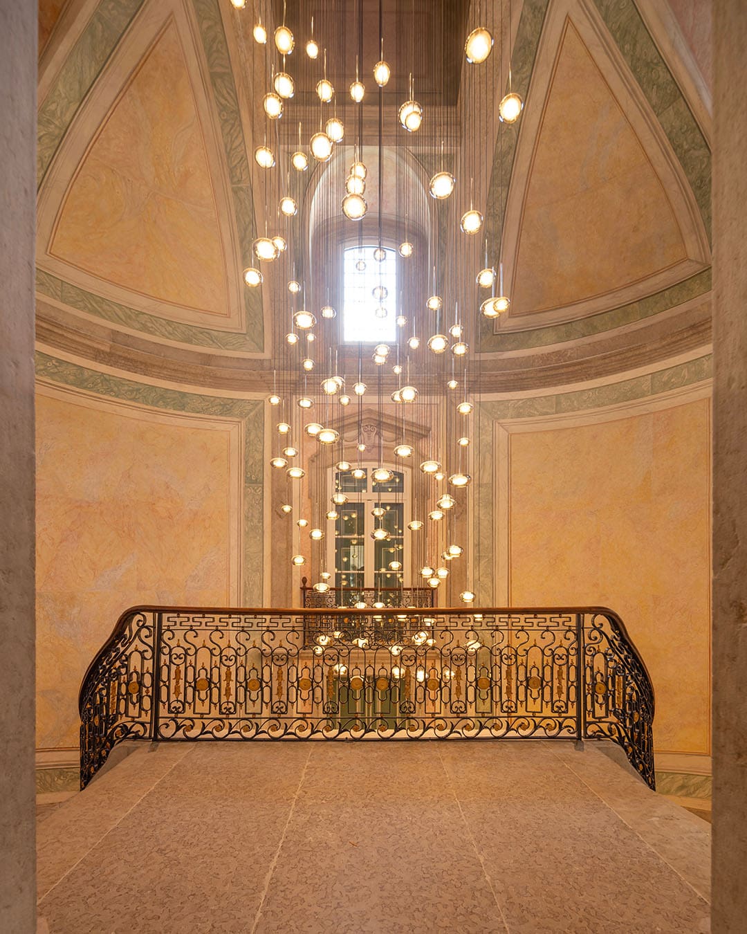 A commissioned light fixing hangs from the celing at the top of a grand flight of staits within the MACAM hotel