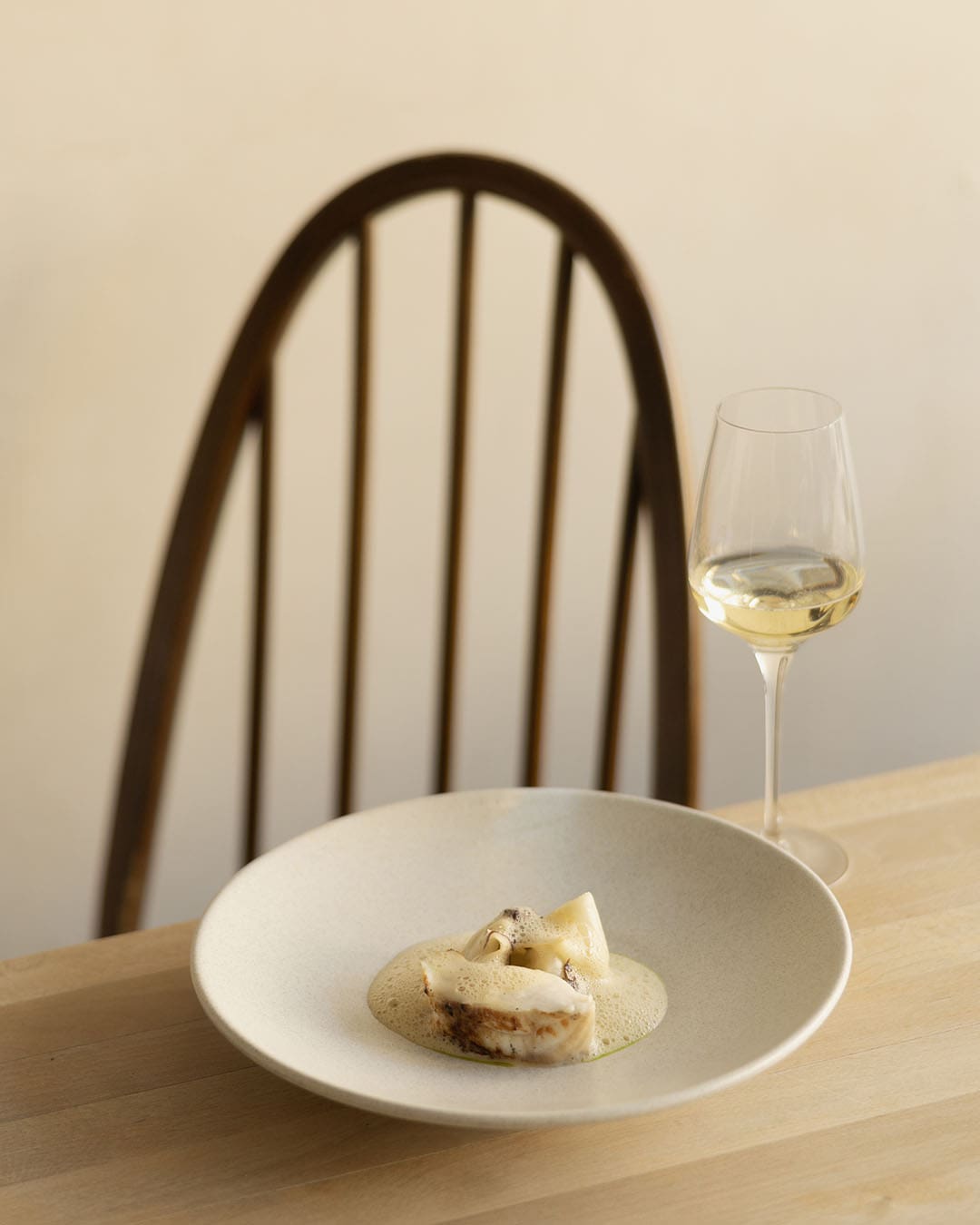 Monkfish in a white bowl and a glass of white wine in a mimimal setting