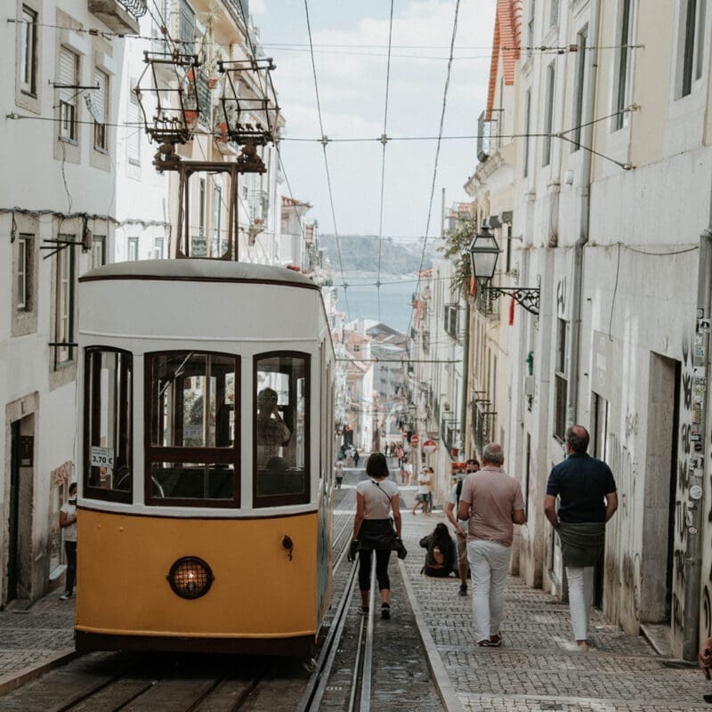 A yellow tram drives down a road in Lisbon
