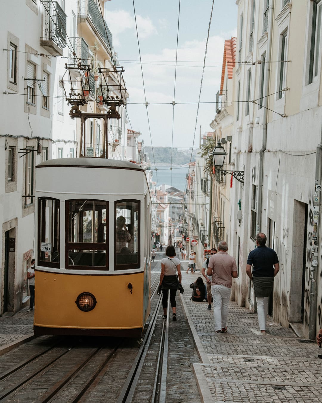 A yellow tram drives down a road in Lisbon