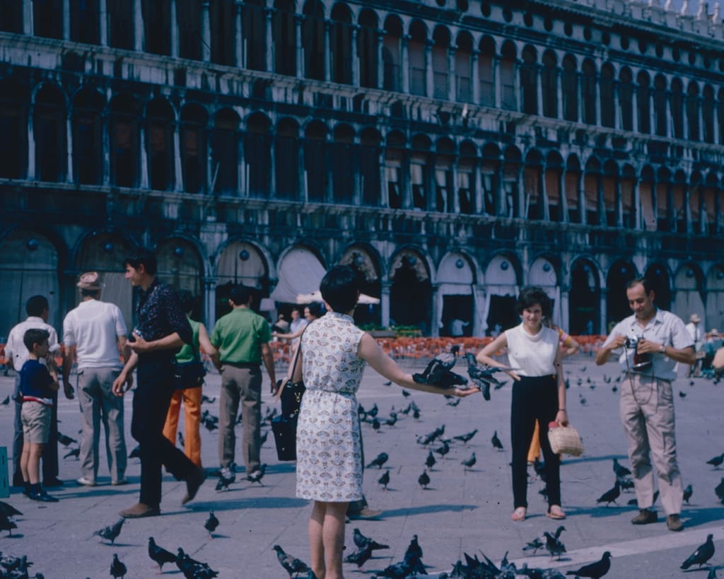 A group of tourists in Venice dancing next to pigeons, circa 1960 