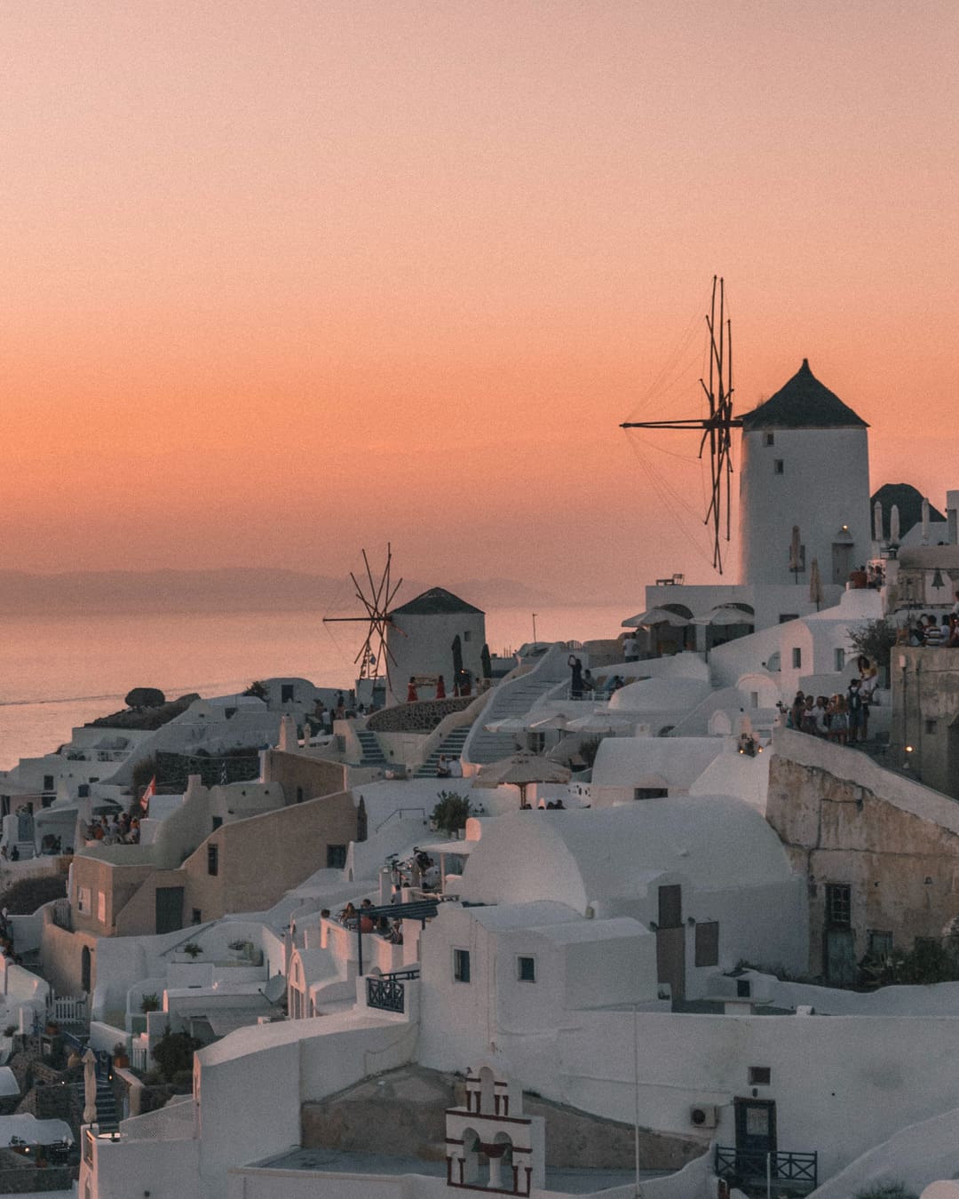 Overtourism in Europe | a peach sky above white buildings in Oia, Greece by Istvan Varro