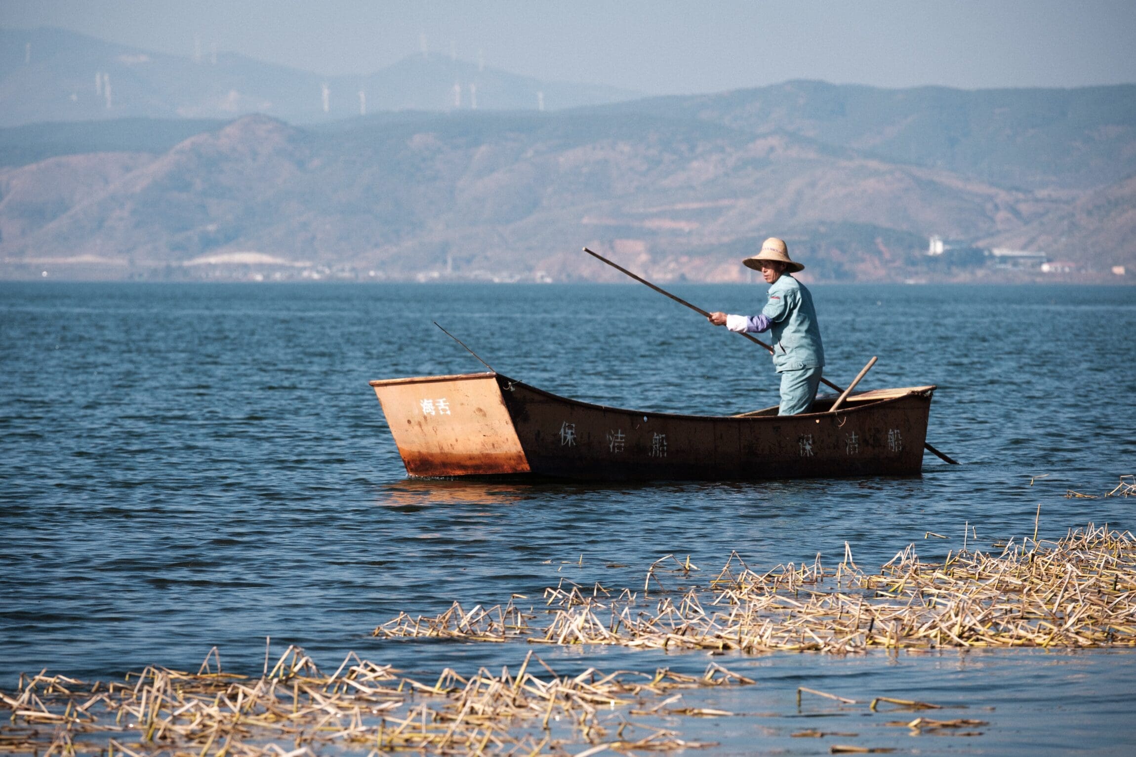 a man on a wooden boat on Erhai Lake in Dali City, photography by Lincoln Yoon